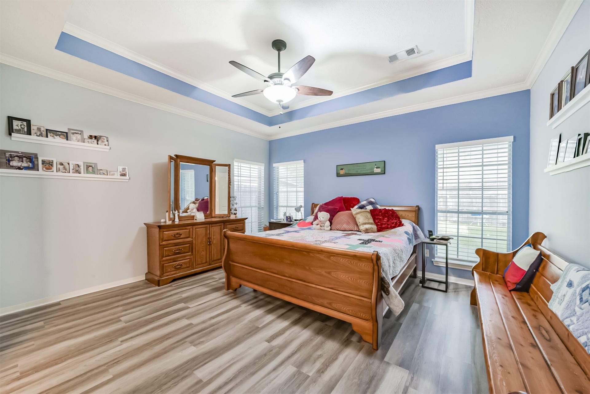 18402 Spinner Court Drive, Humble, TX 77346 The primary bedroom is located on the first floor and features a double coffered ceiling with a ceiling fan and light fixture. Three sets of windows bring ambient lighting to the bedroom.