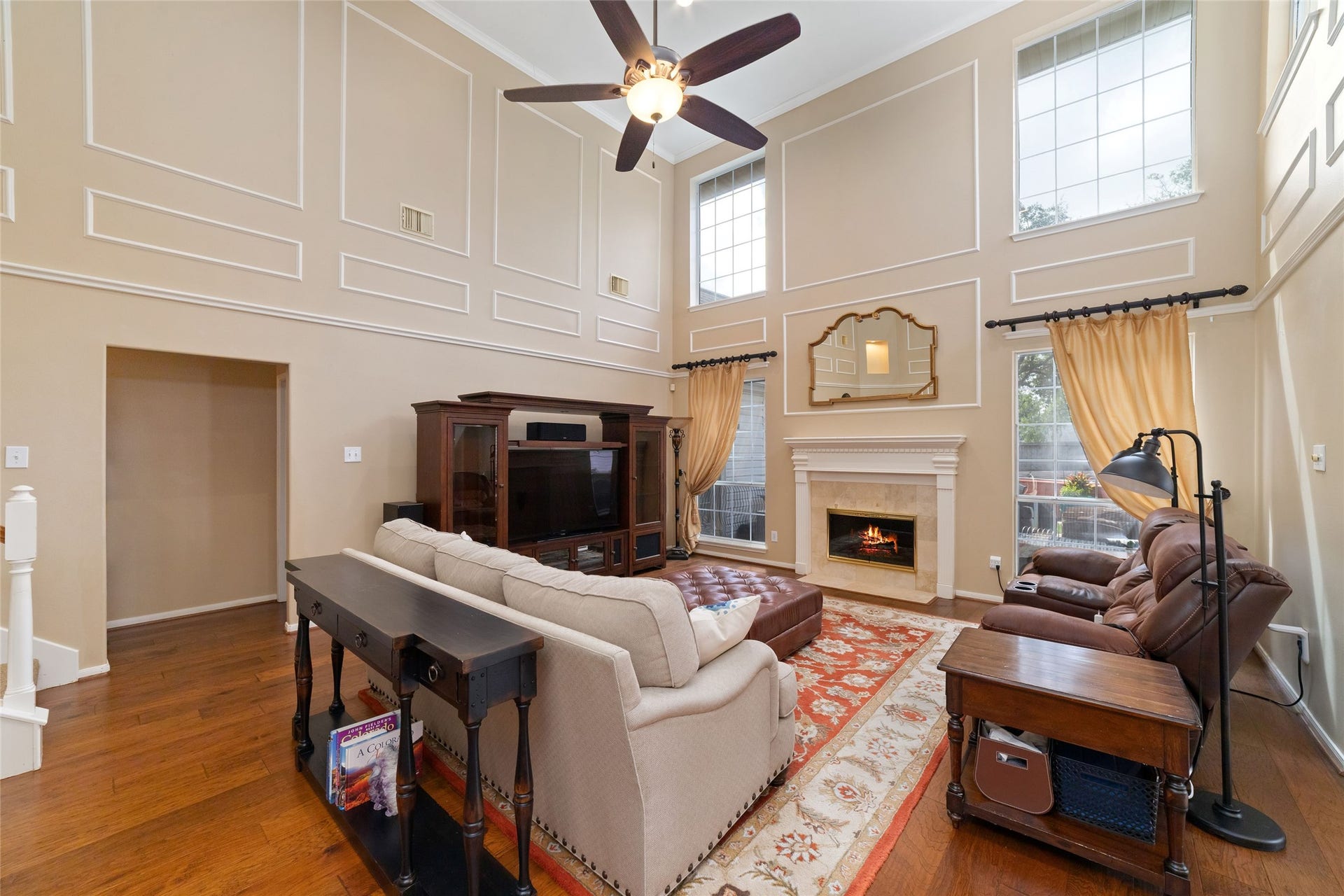 Two-story living room featuring wood flooring, tall windows, architectural molding, and a gas-connected fireplace.