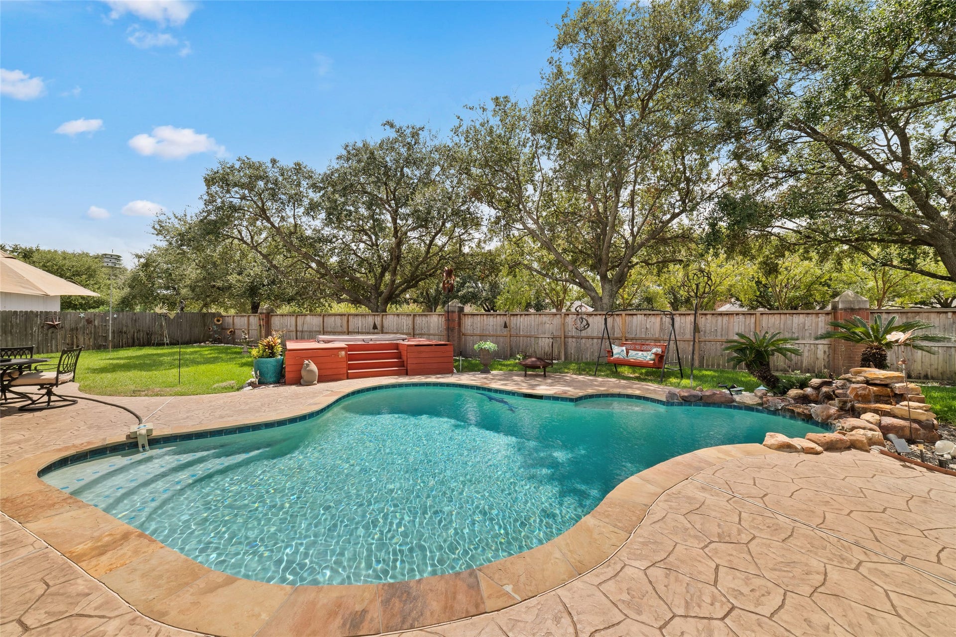 Wide view of the private pool with entry steps, rock water feature, and spacious backyard beyond.