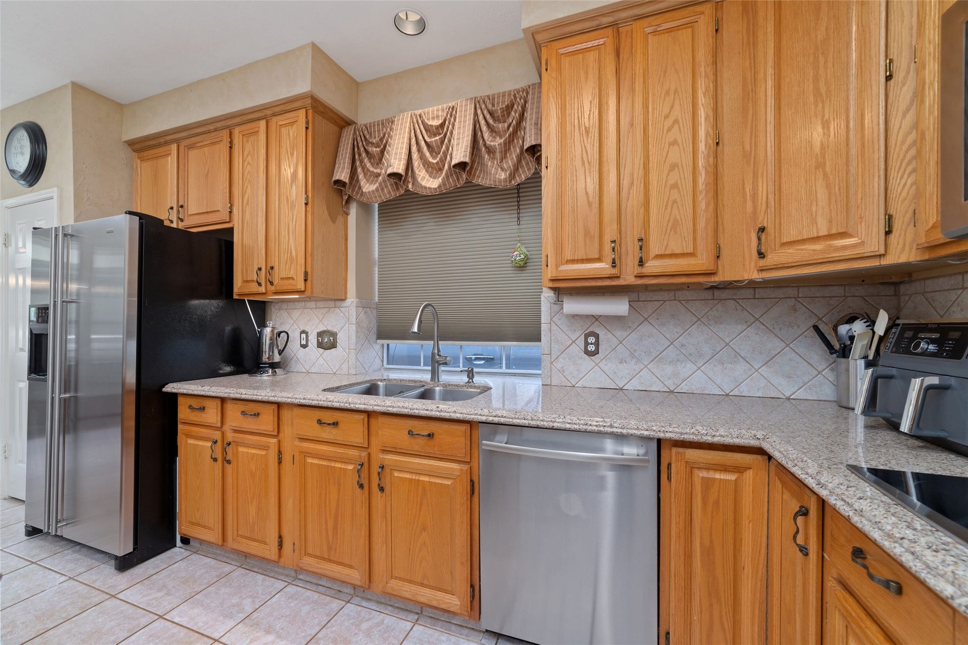 Kitchen work area with granite counters, stainless steel dishwasher, tiled backsplash, and window above the sink.