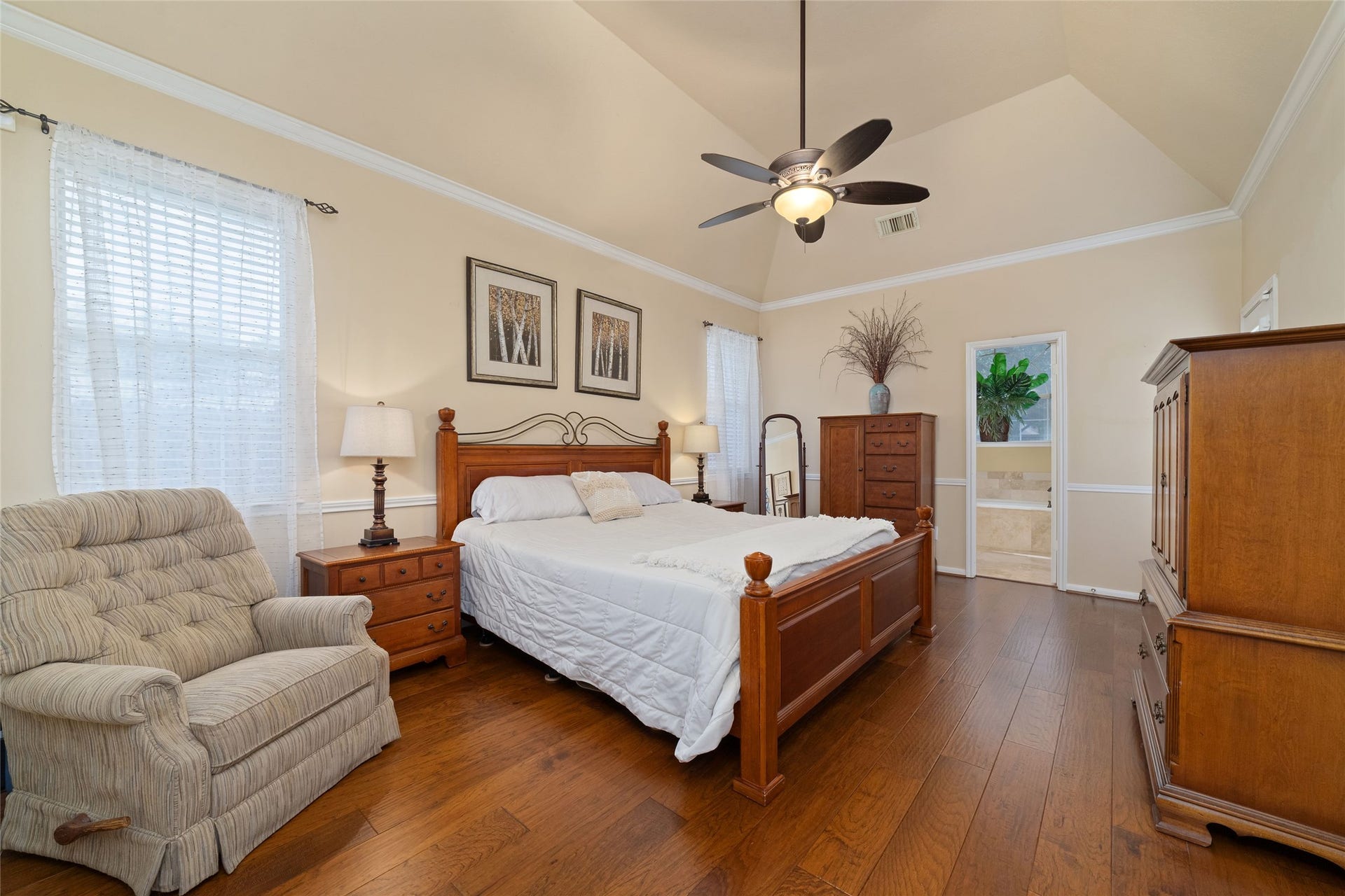 First-floor primary bedroom with wood flooring, tray ceiling, crown molding, and multiple windows.