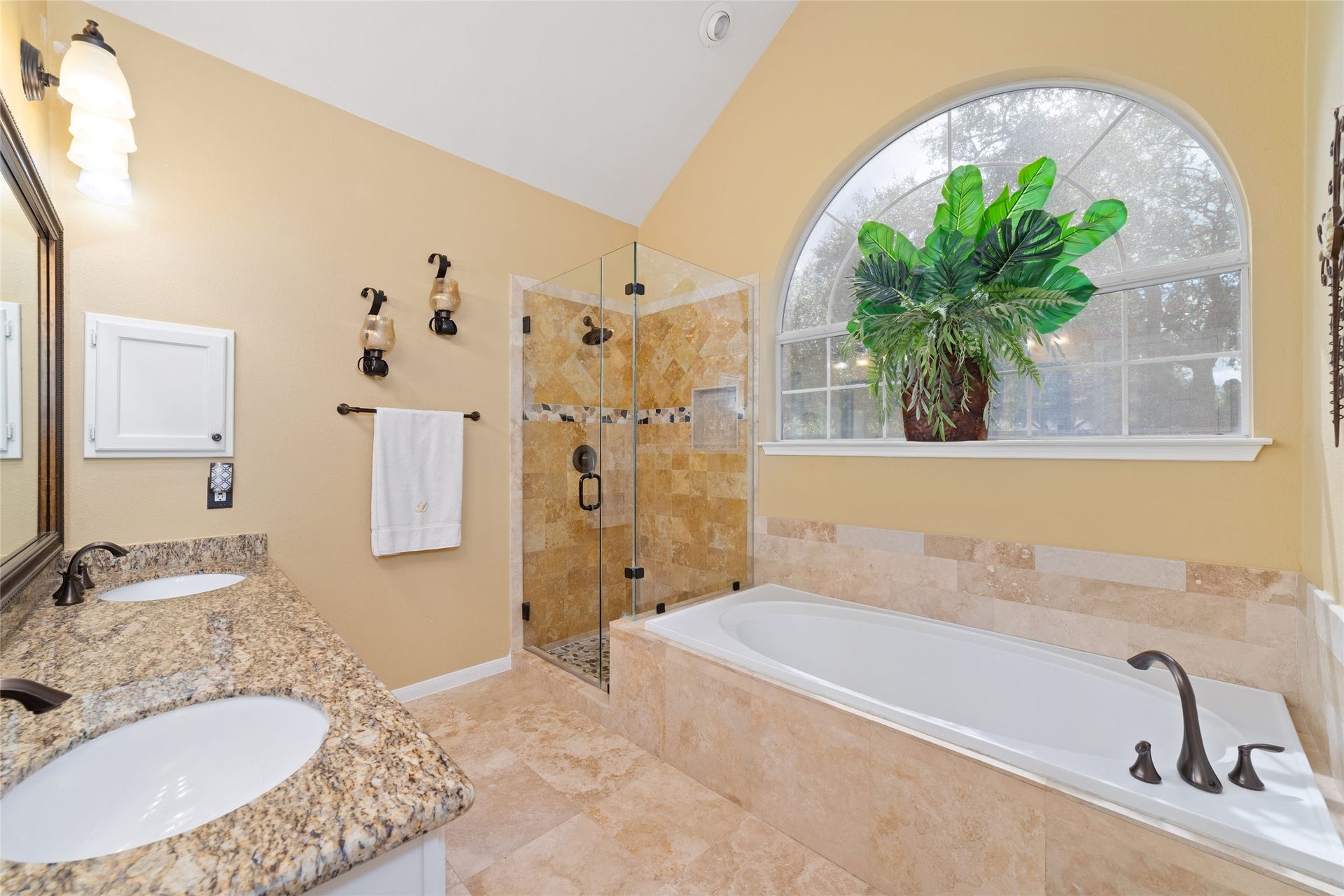 Primary bathroom with dual sinks, granite counters, soaking tub, separate glass-enclosed shower, and arched window.