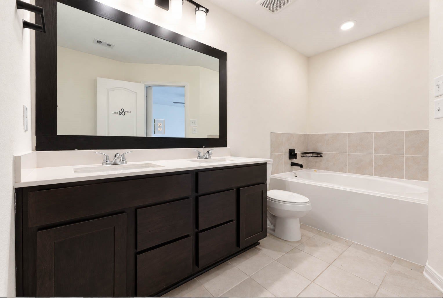 6131 Morning Fern Lane, Humble, TX 77338 The beautifully appointed primary ensuite bath showcases an expansive double-sink vanity with rich espresso-toned cabinetry, generous countertop space, an oversized framed mirror, & stylish contemporary lighting. A luxurious soaking tub with a coordinating tile surround provides the perfect place to relax & unwind.