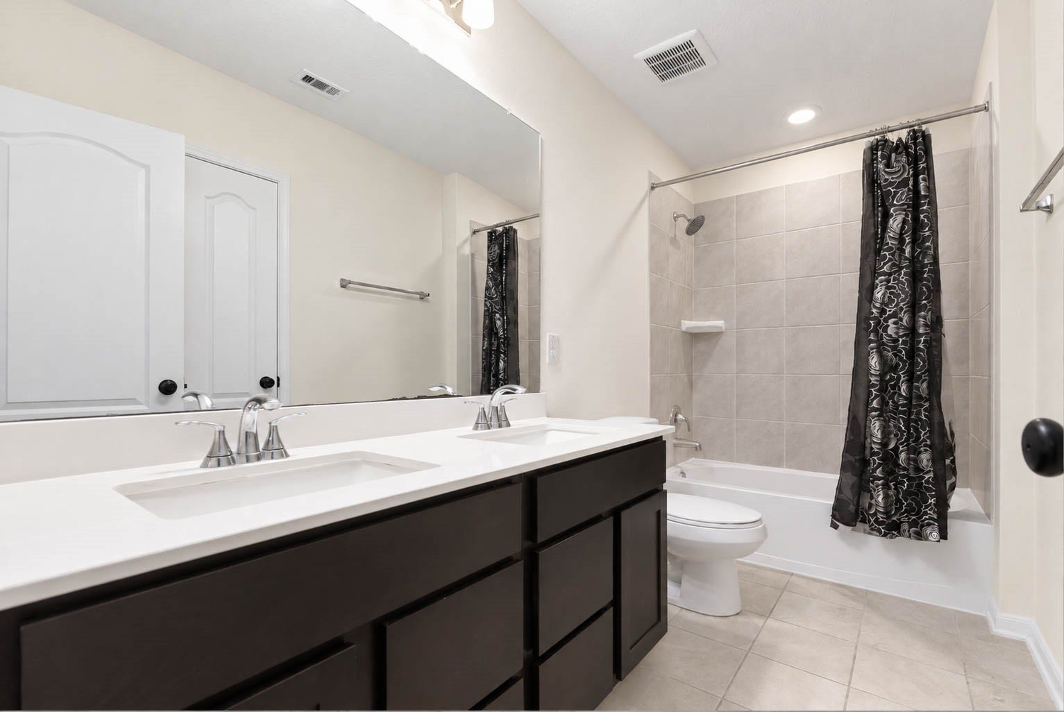 6131 Morning Fern Lane, Humble, TX 77338 The spacious secondary bathroom features a generous double-sink vanity with crisp white countertops, rich espresso-toned cabinetry, & a a large mirror. Stylish brushed-nickel fixtures, overhead vanity lighting, neutral tile flooring, & a tub/shower combination with coordinating tile surround complete this space.