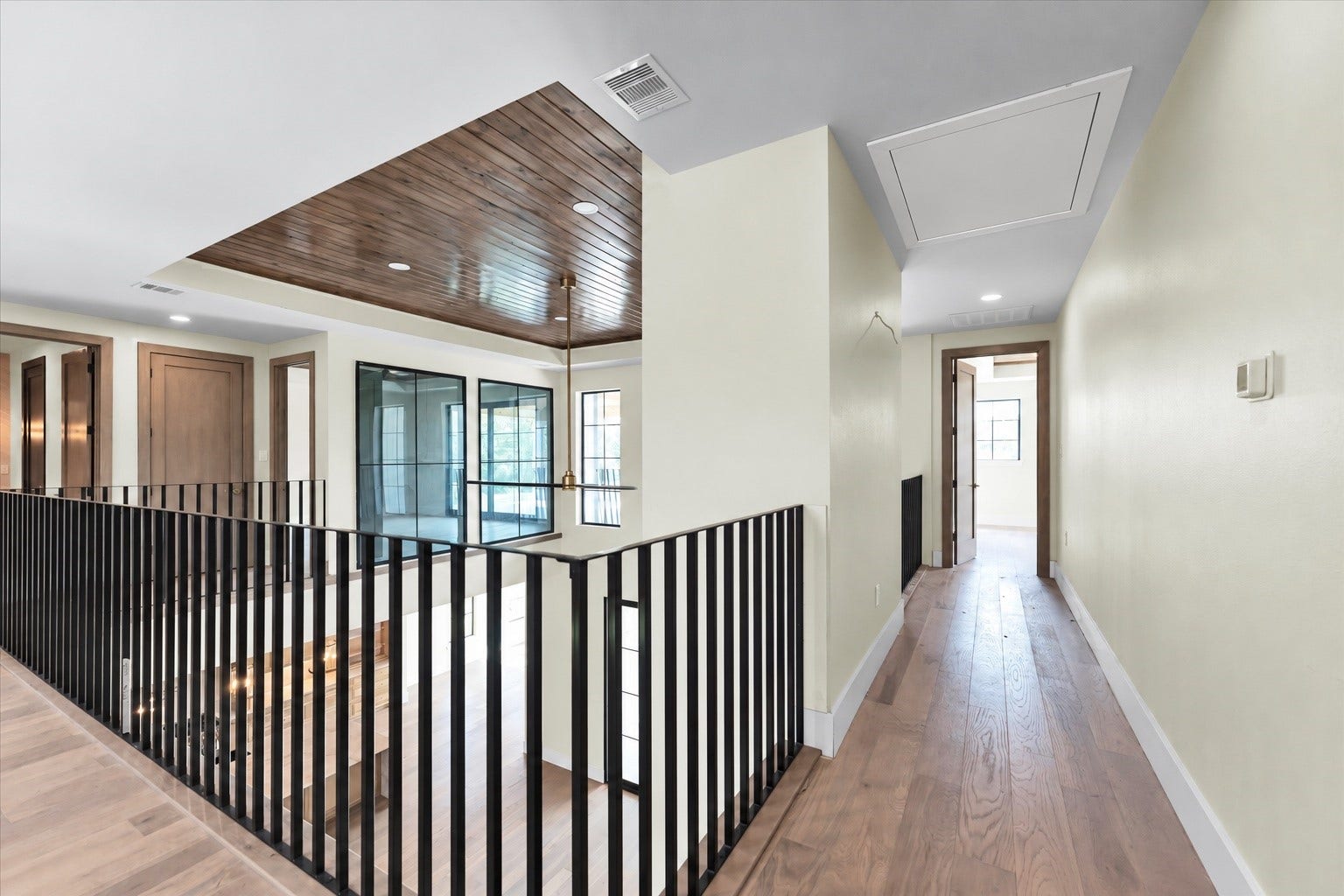 23701 Birch Grove Road, Montgomery, TX 77316 Elegant hallway with sleek black railings, warm wood accents, and ample natural light from large windows.