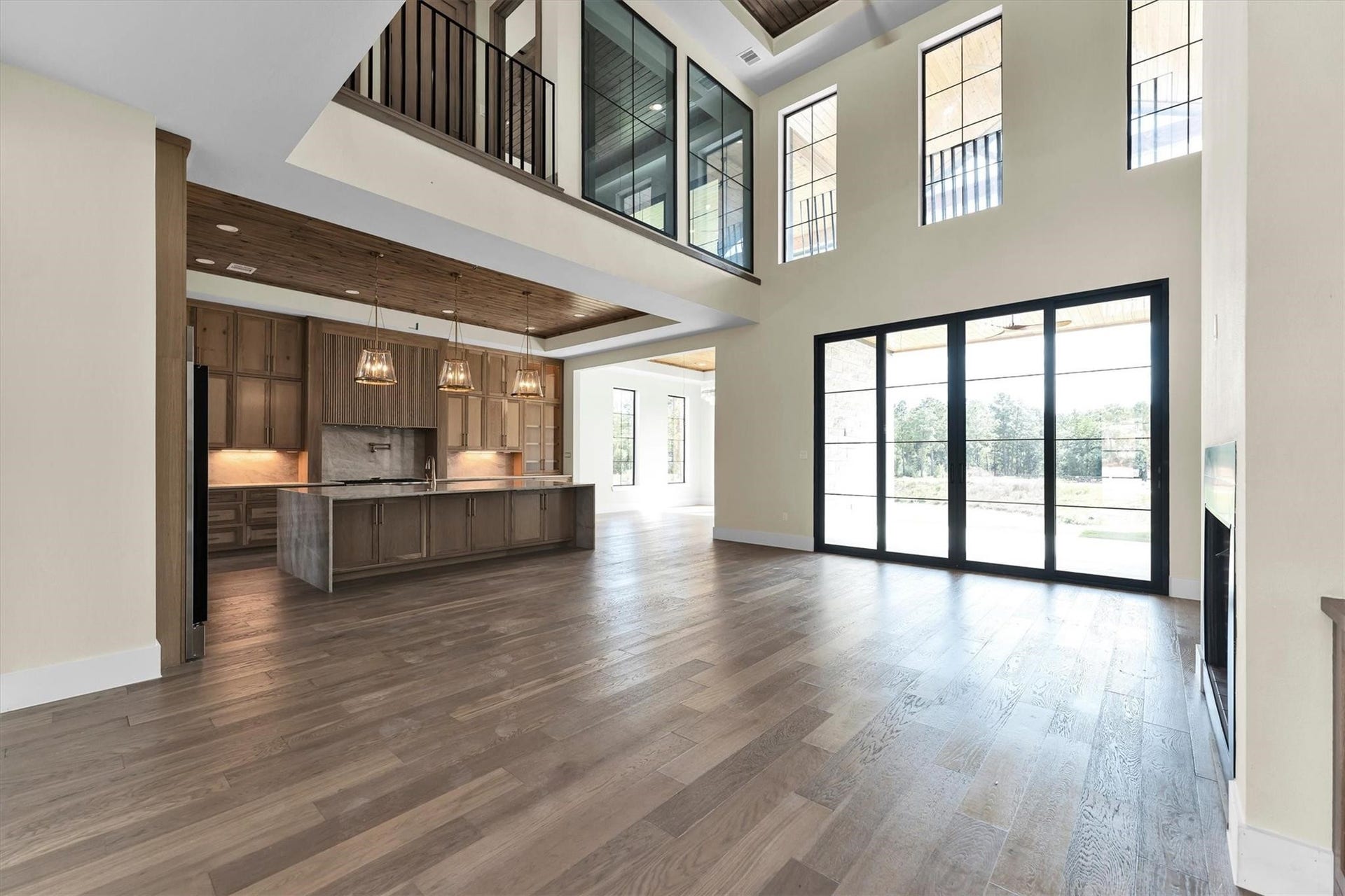 23701 Birch Grove Road, Montgomery, TX 77316 Stunning open-concept living area with soaring ceilings and expansive windows, flooding the space with natural light. The modern kitchen features a large island and elegant pendant lighting, seamlessly integrated into the spacious design.