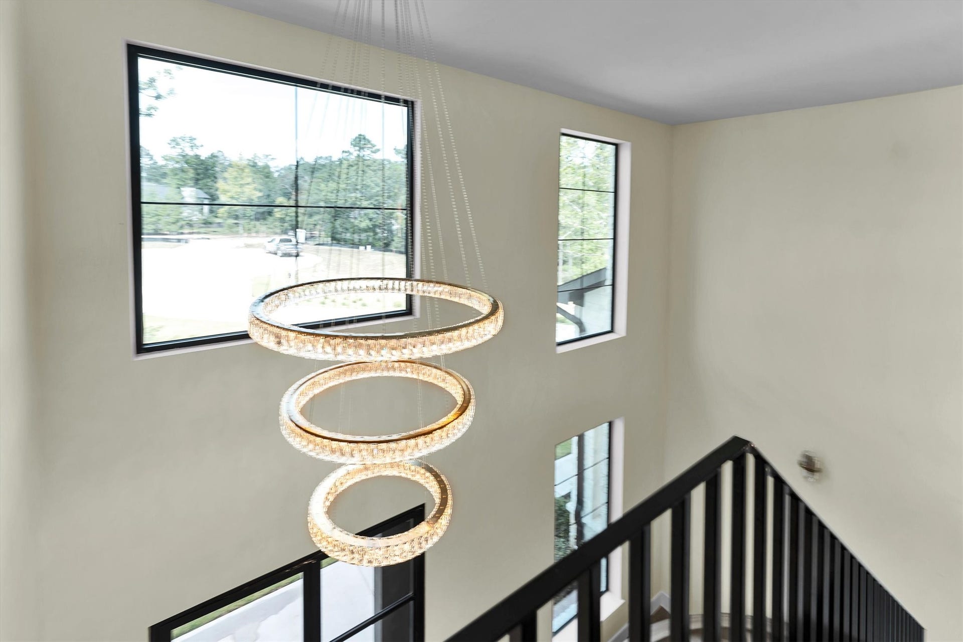 23701 Birch Grove Road, Montgomery, TX 77316 Elegant staircase with a sleek black railing, illuminated by a stunning modern chandelier, and framed by large windows that fill the space with natural light.