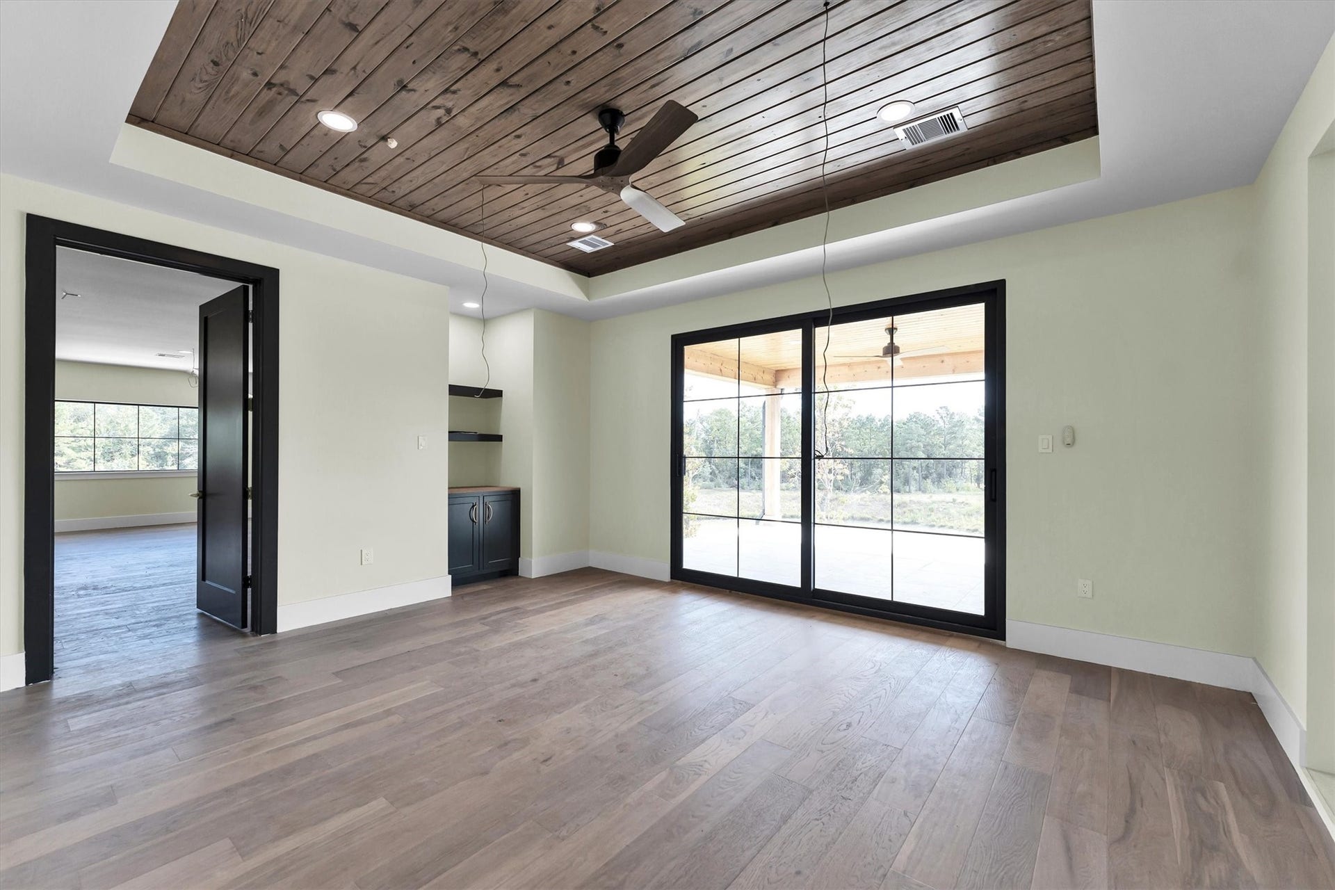 23701 Birch Grove Road, Montgomery, TX 77316 Spacious room with elegant wood flooring and a stunning wood-paneled ceiling featuring recessed lighting and a ceiling fan. Large sliding glass doors open to an inviting outdoor view, complemented by a convenient wet bar area and adjacent access to another room.