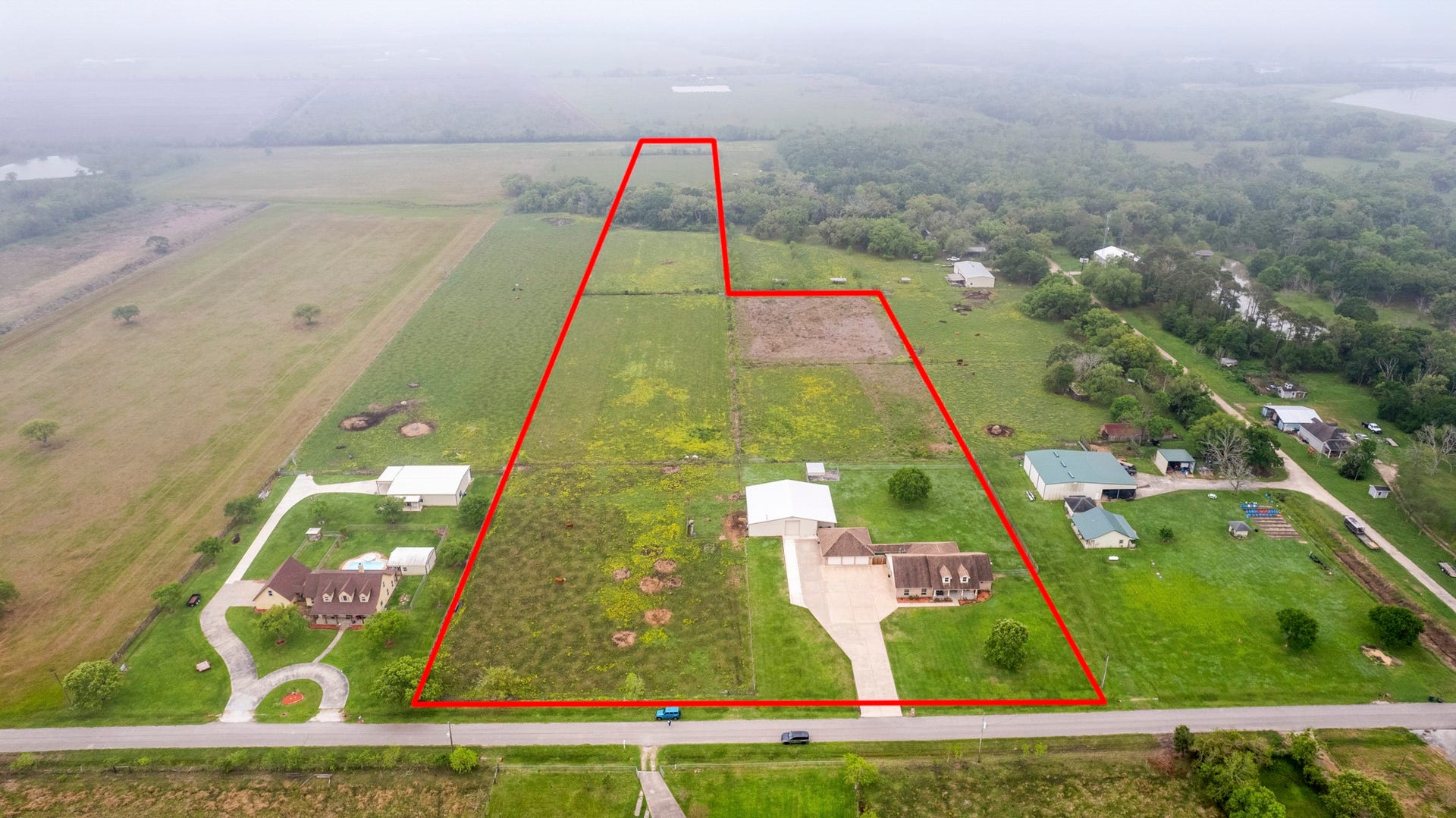 Aerial view showcasing the full 14.23 acres, outlined in red, featuring expansive fenced and cross-fenced pastures, a beautiful brick home, spacious garage, large workshop, and Austin Bayou running through the rear acreage