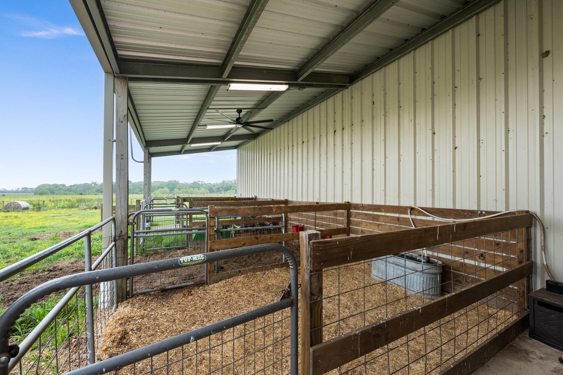 Covered livestock stalls featuring metal fencing, gated access, and a sheltered area for horses or cattle, with convenient access to the surrounding pastures.