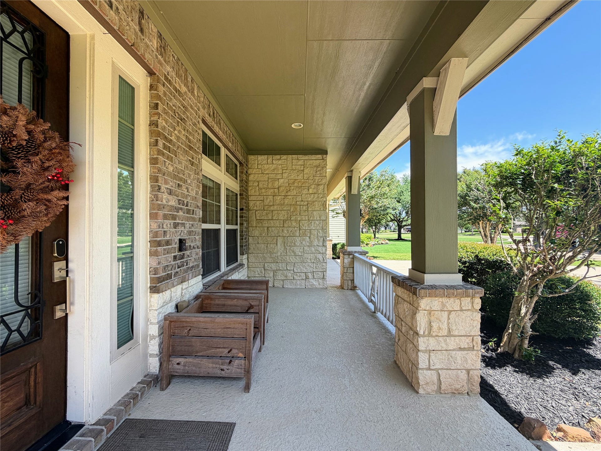 5119 Water Oak Crescent, Fulshear, TX 77441 This covered front porch offers the perfect space to relax, highlighting a custom glass-inlaid front door, robust stone pillars, elegant brick accents, and a tranquil view of the beautifully landscaped front yard.