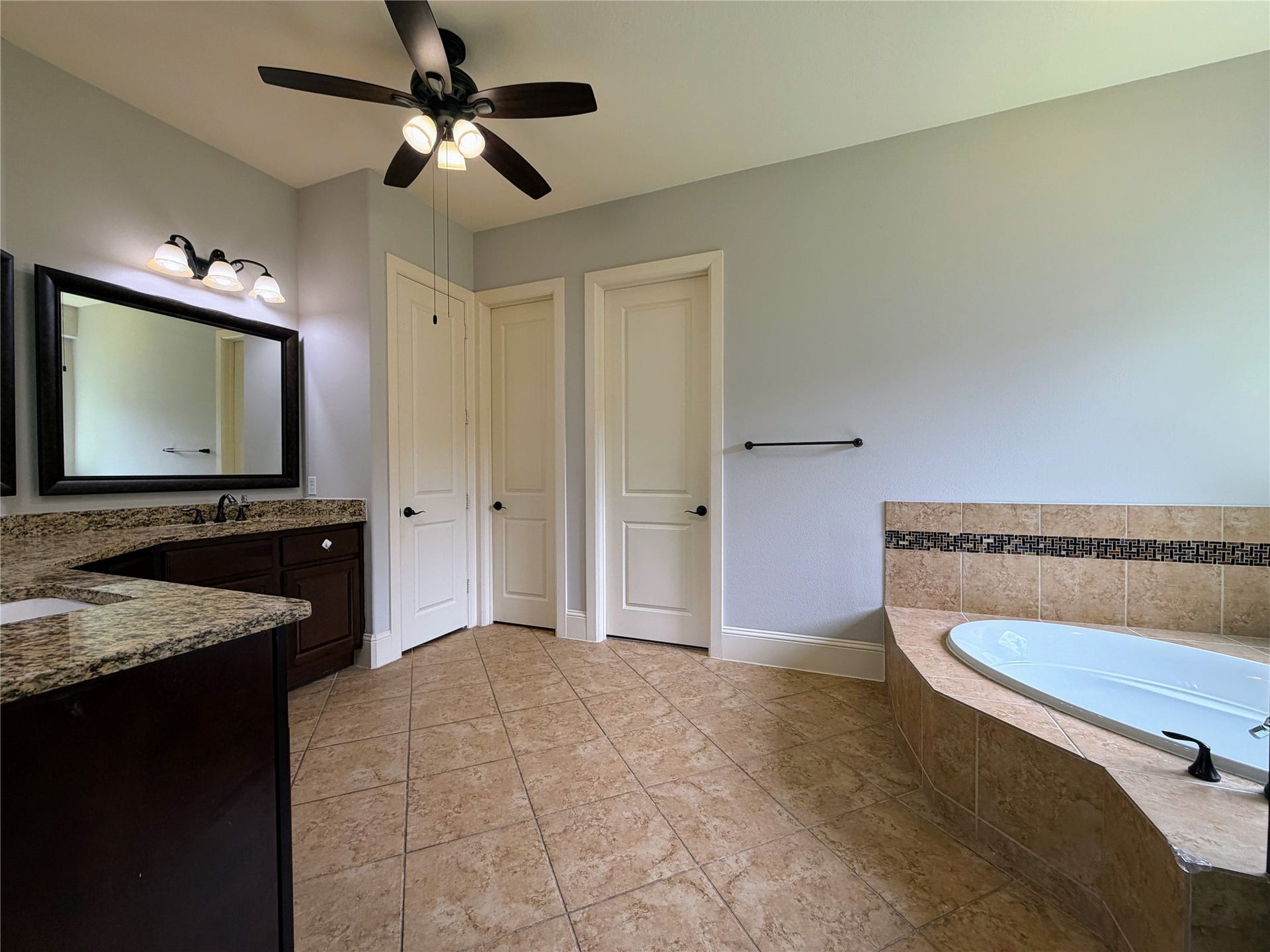 5119 Water Oak Crescent, Fulshear, TX 77441 Spa-like primary bath! Indulge in the deep corner soaking tub with elegant tile detailing. Features a massive granite-topped vanity with dual sinks, rich wood cabinetry, a large framed mirror, stylish lighting, and a massive walk-in layout.