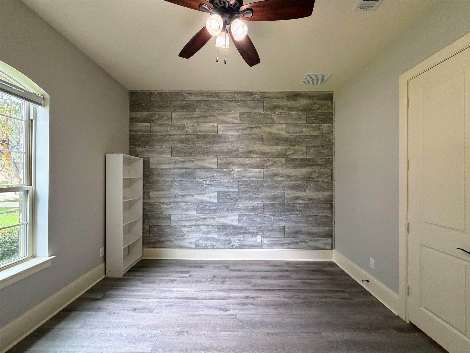 5119 Water Oak Crescent, Fulshear, TX 77441 Versatile downstairs guest bedroom! Showcases a stunning rustic wood-plank accent wall, modern wood-look flooring, a stylish ceiling fan, and an arched window providing natural light and serene front-yard views.