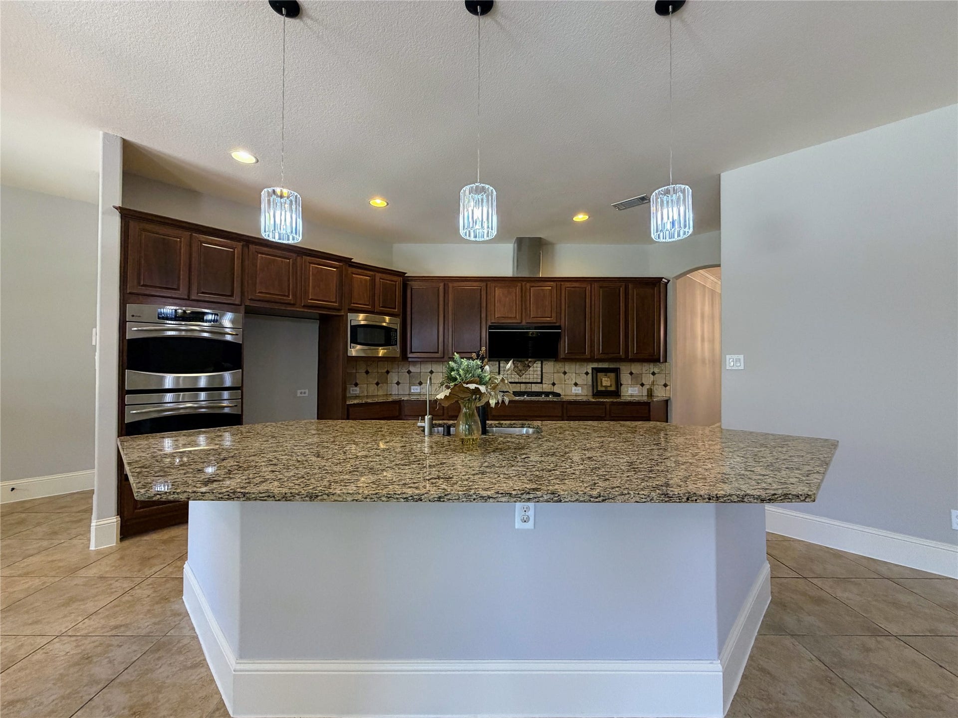 5119 Water Oak Crescent, Fulshear, TX 77441 Chefs dream kitchen! Features an oversized granite island with modern pendant lights, beautiful wood cabinetry, a tile backsplash, and high-end stainless steel appliances including a double wall oven and built-in microwave.