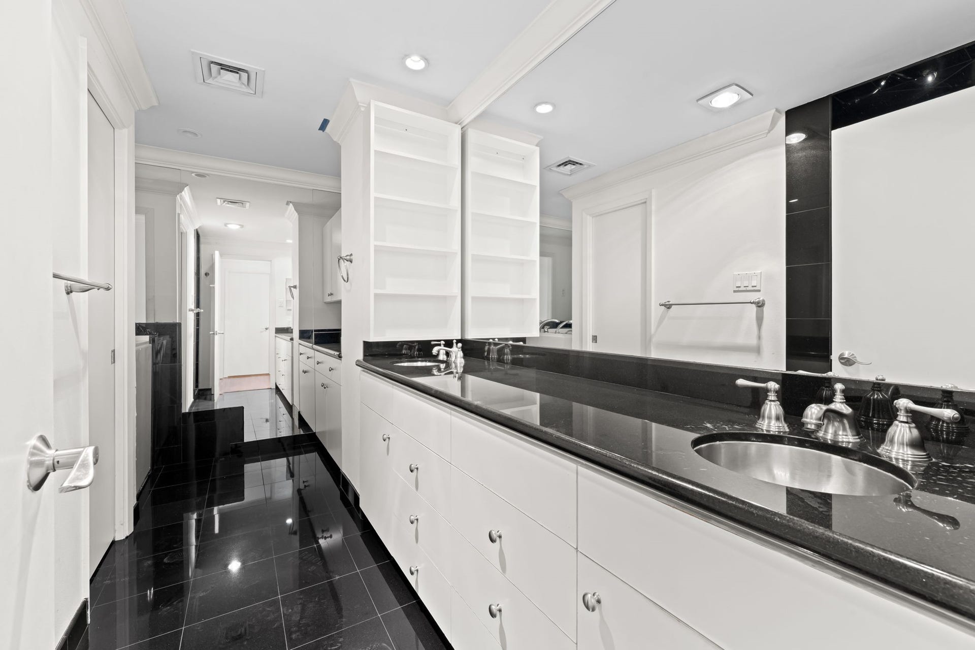 A long vanity offers plentiful counter space and storage beneath a wall of mirrors. The updated primary bathroom balances dramatic contrast with a sophisticated, polished aesthetic.