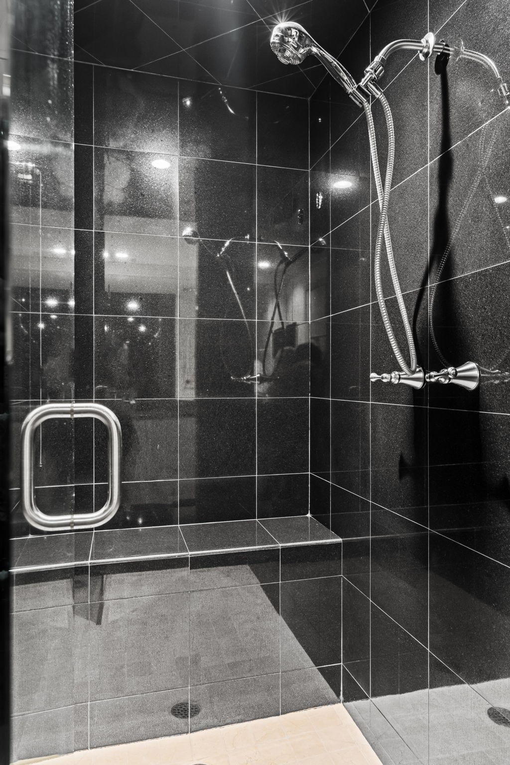 The extra-large shower is finished in striking dark stone and enclosed with glass. Multiple fixtures and generous proportions contribute to a spa-inspired experience.