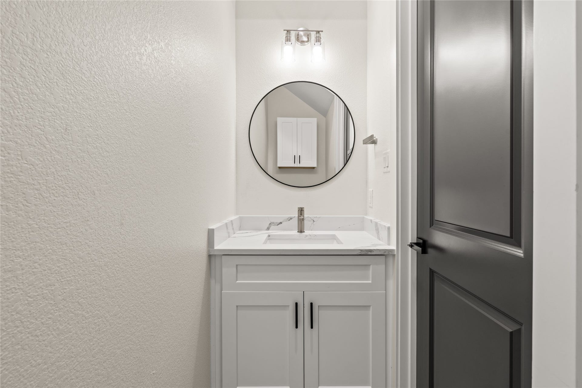 4521 Newberry Street, Houston, TX 77051 Main floor powder room quartz vanity, sleek round black mirror, modern vanity light, and custom dark accent door.