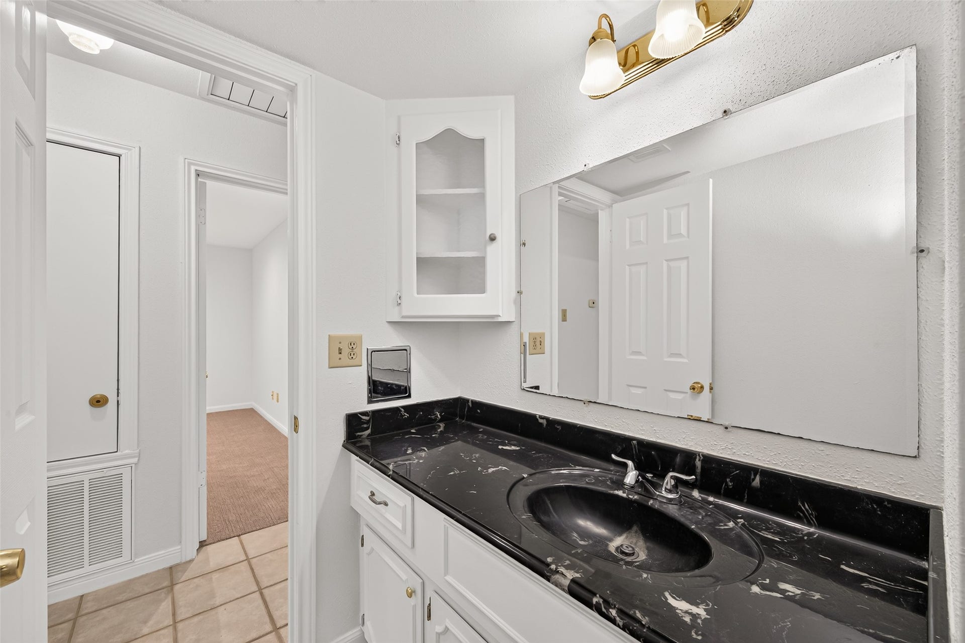 7602 Salge Drive, Houston, TX 77040 Well-appointed secondary bathroom featuring a striking black marble-look vanity countertop, white cabinetry, a spacious mirror, and decorative lighting. A built-in glass-front cabinet provides additional storage, while neutral tile flooring completes the space.