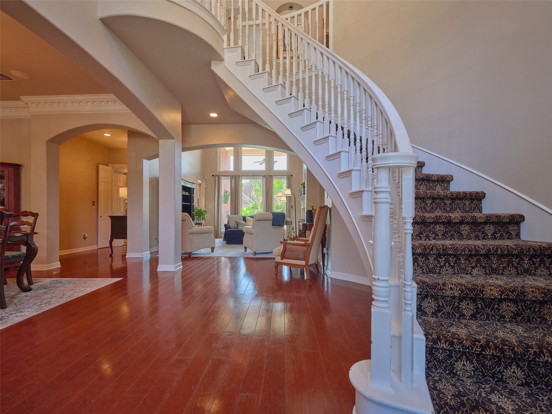 7111 Mohave Hills, Houston, TX 77069 Elegant curved staircase with ornate detailing leads to a spacious living area, featuring rich hardwood floors and abundant natural light.