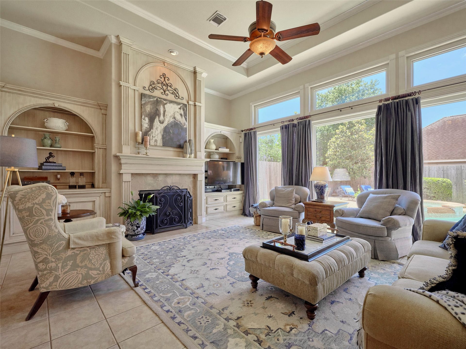 7111 Mohave Hills, Houston, TX 77069 Bright and inviting living room with large windows, elegant built-in shelving, and a cozy fireplace, perfect for relaxing or entertaining.