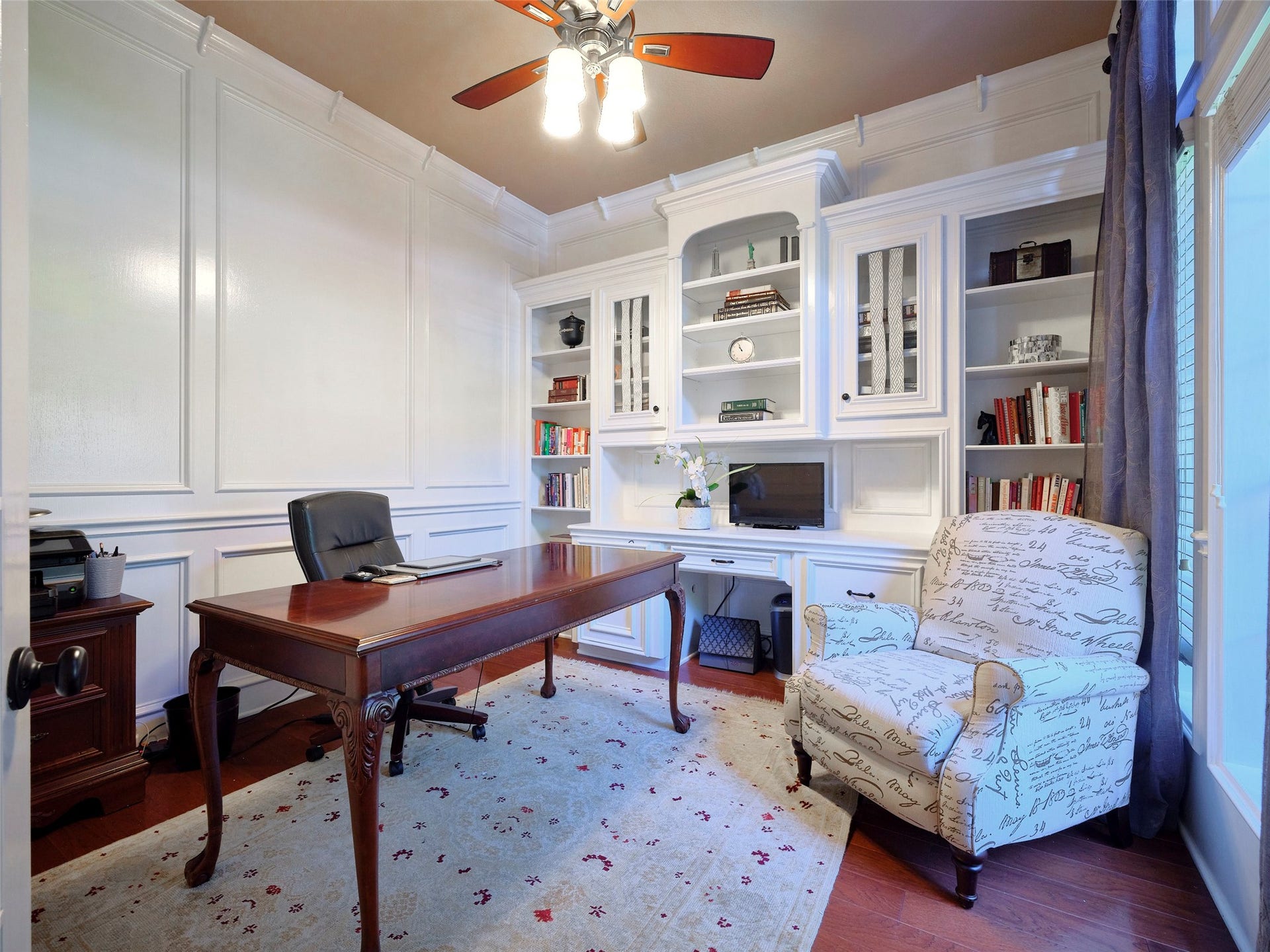 7111 Mohave Hills, Houston, TX 77069 Elegant home office featuring custom built-in shelving, a spacious wooden desk, and a cozy armchair, enhanced by rich wood flooring and abundant natural light.