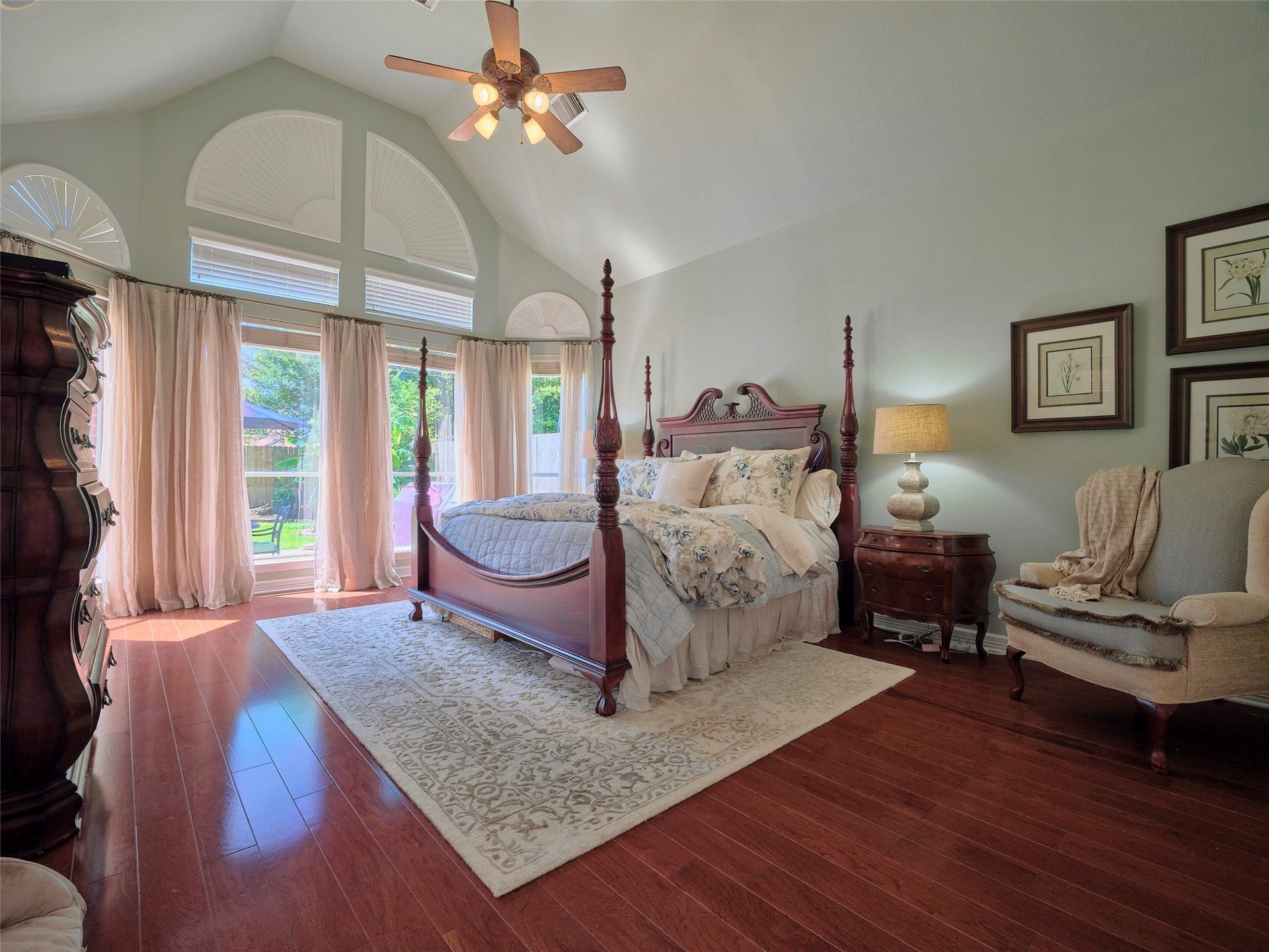 7111 Mohave Hills, Houston, TX 77069 Elegant primary bedroom featuring a vaulted ceiling, abundant natural light through large arched windows, and a luxurious four-poster bed complemented by rich hardwood floors.