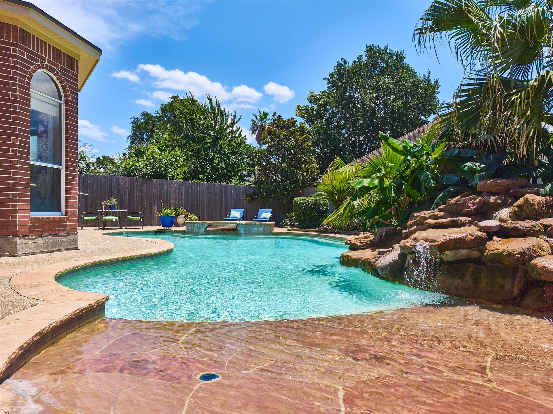 7111 Mohave Hills, Houston, TX 77069 Enjoy a tropical oasis in your backyard with a sparkling pool, natural rock waterfall, and lush landscaping, perfect for relaxation and entertaining.