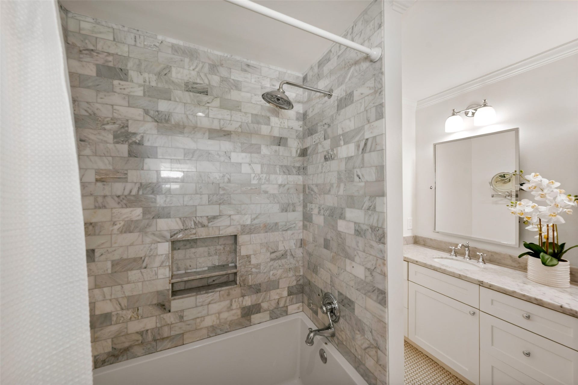 1343 Del Norte Street, Houston, TX 77018 Detailed view of the primary baths marble-tiled tub/shower surround, complete with a built-in niche and rain-style showerhead.