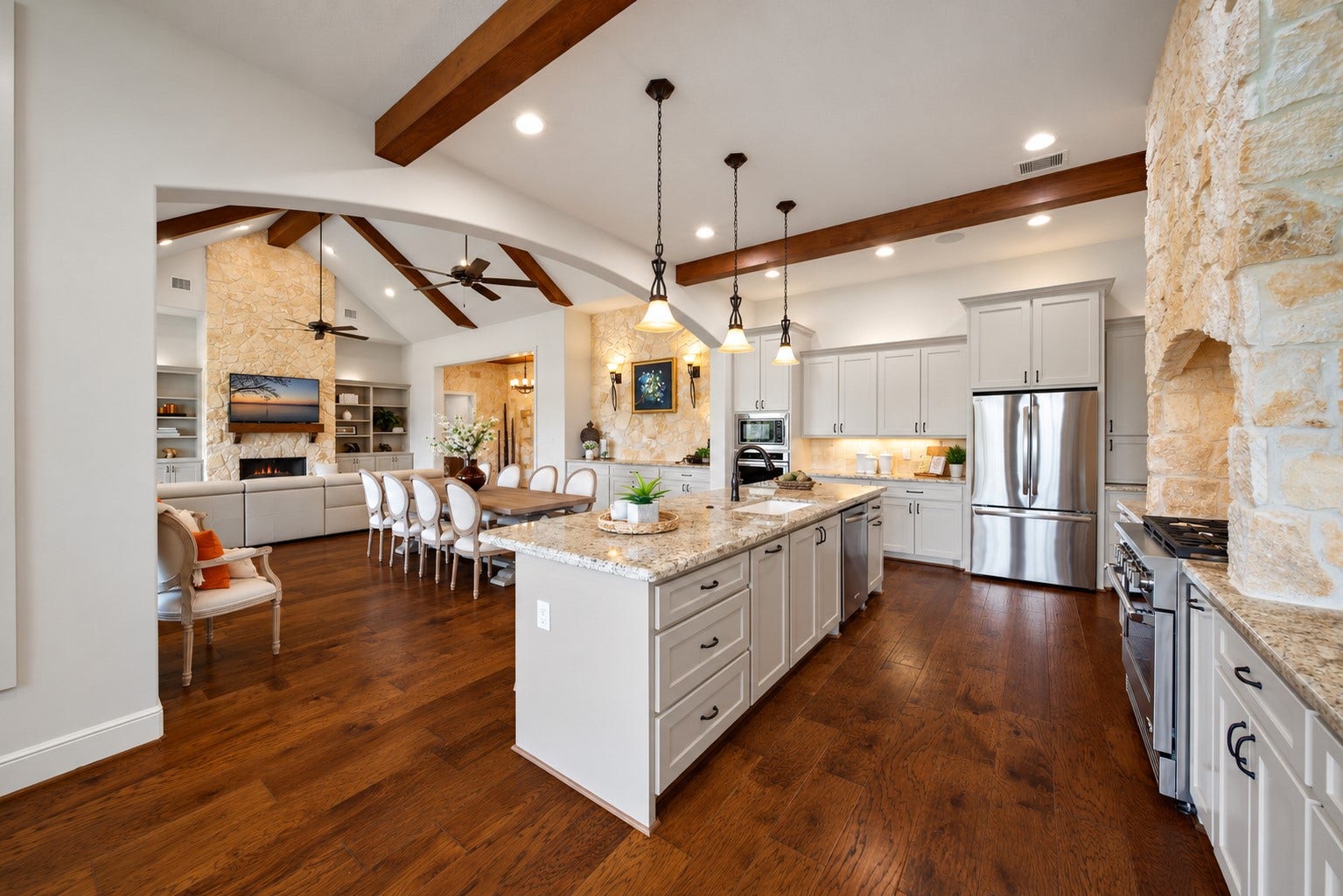 The kitchen handles the work while welcoming the gathering. Granite counters, double ovens and abundant cabinetry support the meal, with the dining and living areas just beyond.