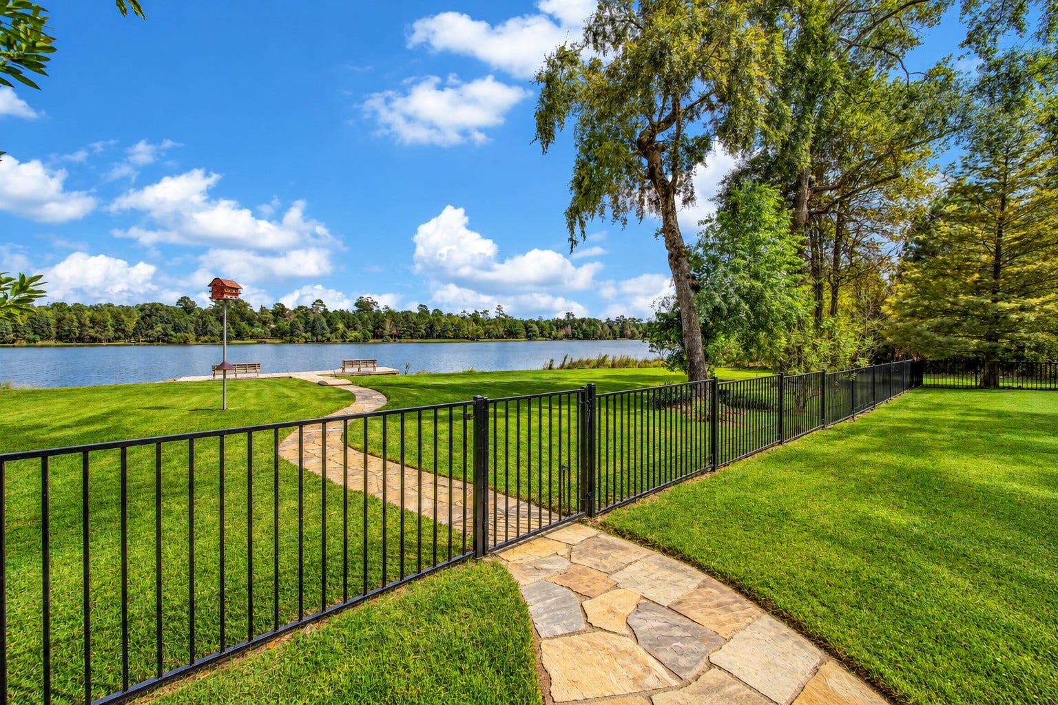Beyond the fenced backyard, the landscape opens to the lake. A stone path draws the eye toward the shoreline, giving the water a place in the home's everyday story.