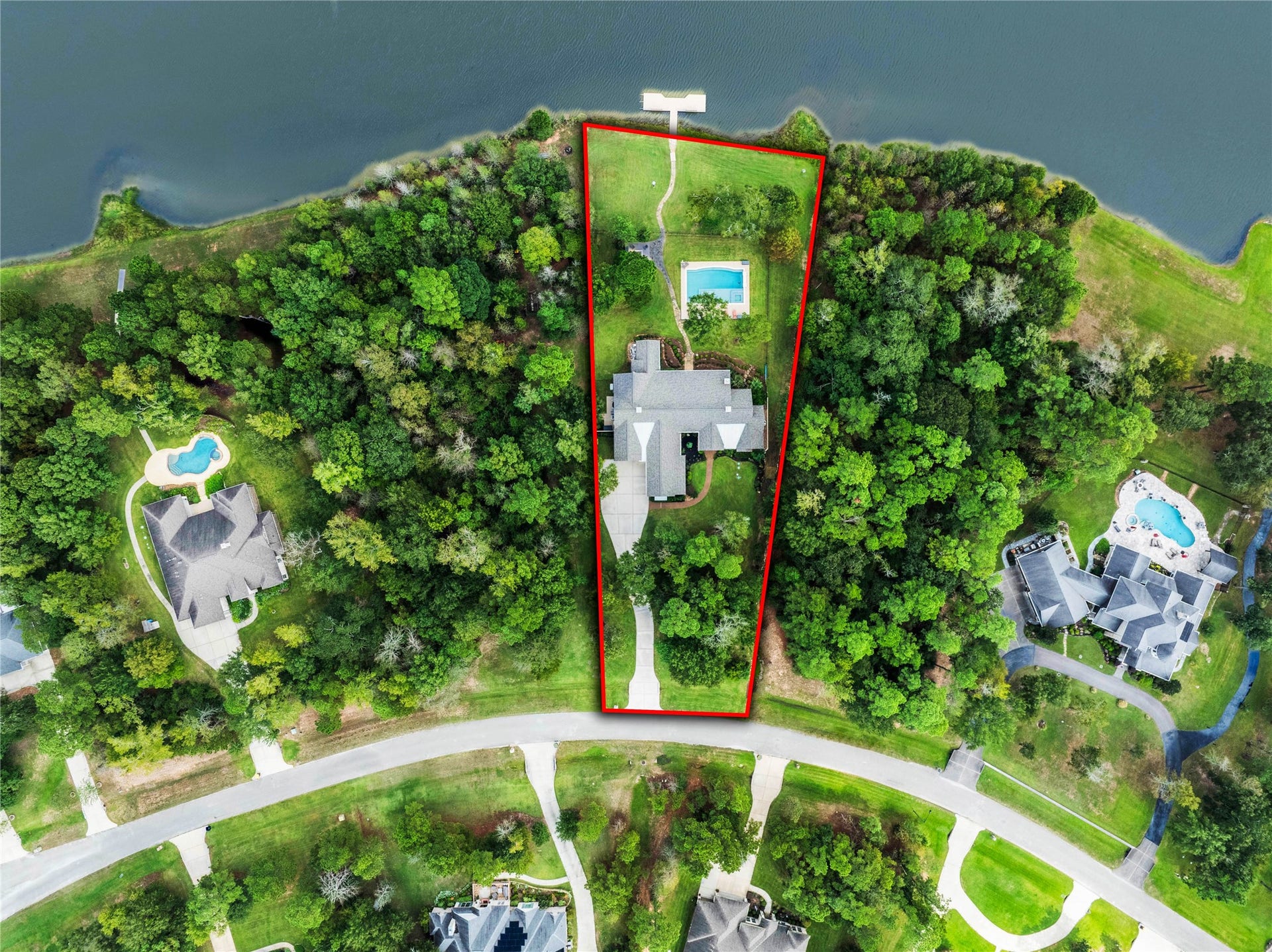 The aerial introduces the full setting:  the home near the street, the pool behind it and the lake along the rear of the property. The approximately 1.23-acre parcel is outlined for reference.