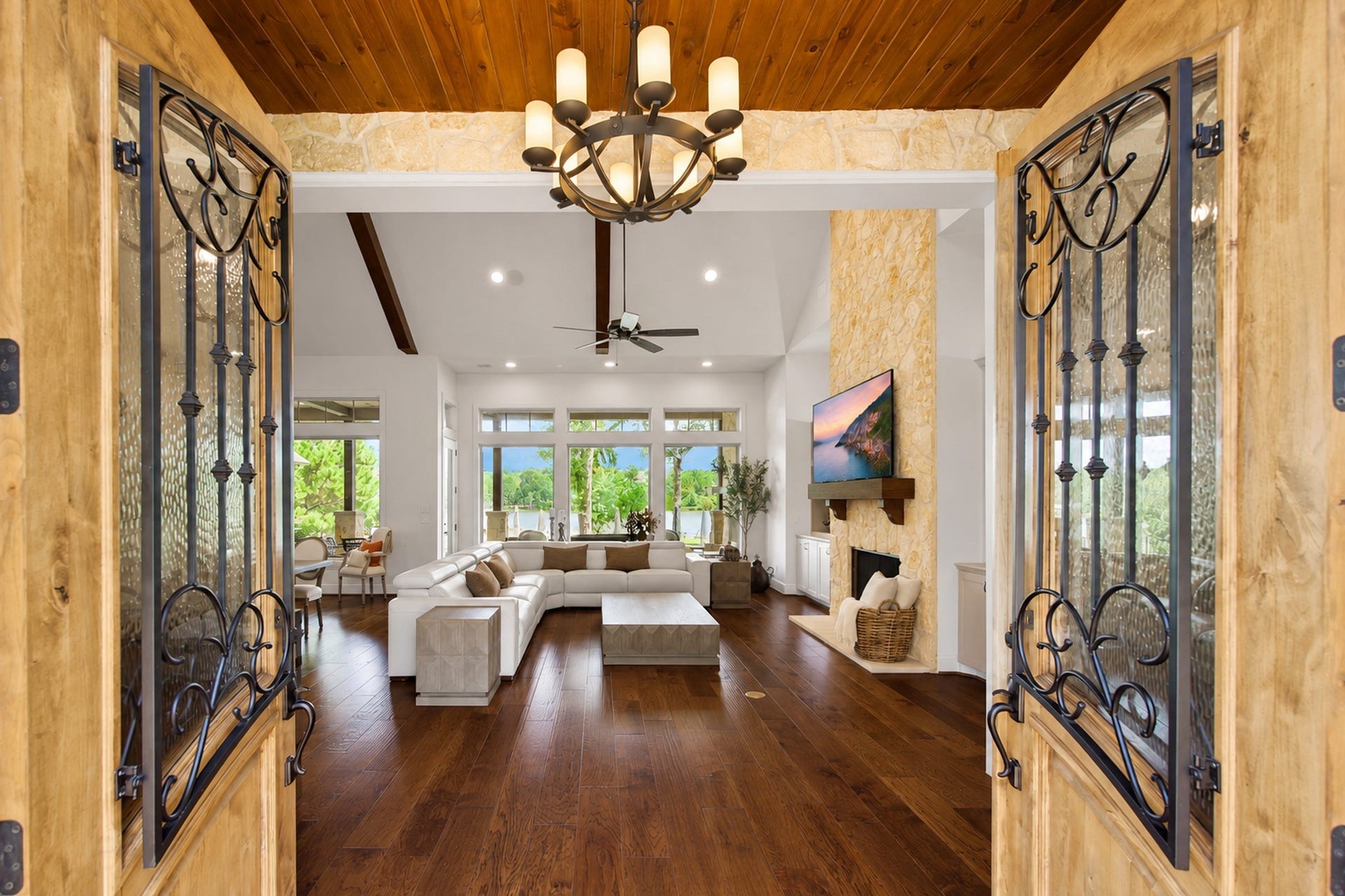 Open the doors and the home draws you toward the living room and the greenery beyond. Wood floors, stonework and an open sightline make the arrival feel warm and welcoming.