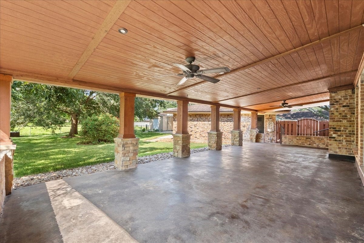 802 Riverside Drive, Alvin, TX 77511 Expansive covered patio with ceiling fans and stone pillars, overlooking a lush green yard, perfect for outdoor entertaining.