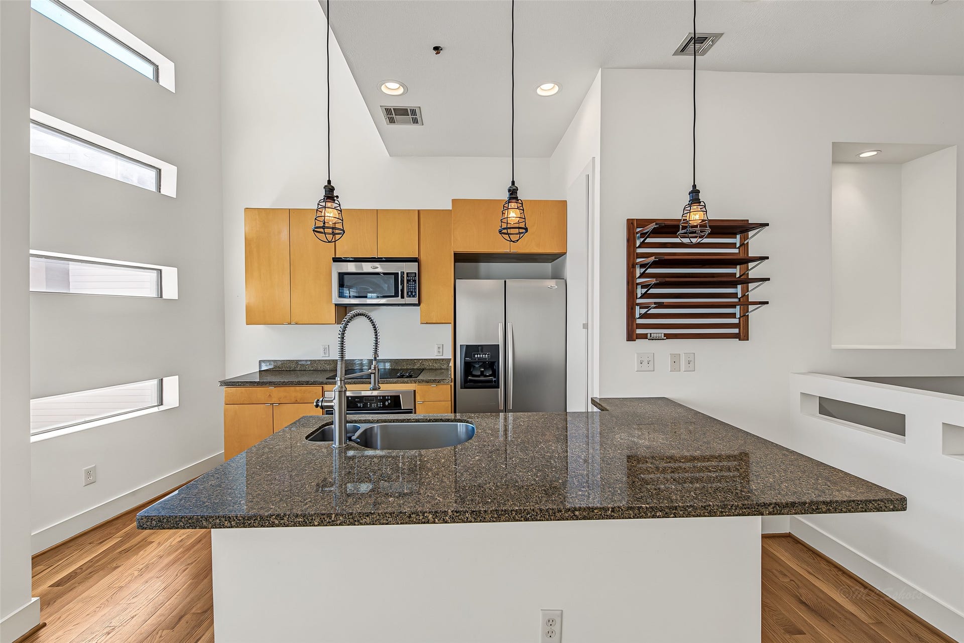 1555 Birdsall Street, #A, Houston, TX 77007 The chef's kitchen boasts a large granite island with breakfast bar seating, industrial cage pendant lighting, and warm natural wood cabinetry.