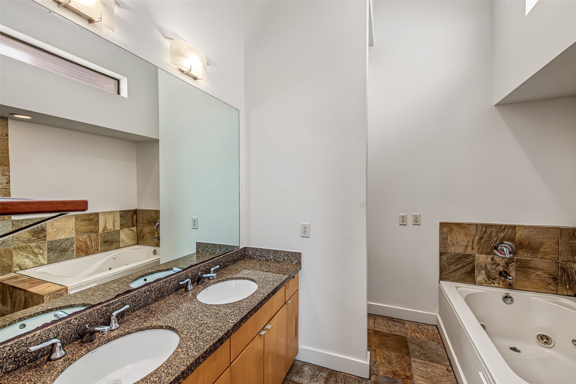 1555 Birdsall Street, #A, Houston, TX 77007 Indulge in the spa-like primary bathroom featuring double granite vanity sinks, and natural wood cabinetry. Soaring ceilings and high transom windows fill the space with soft daylight, creating a private retreat to unwind and recharge.
