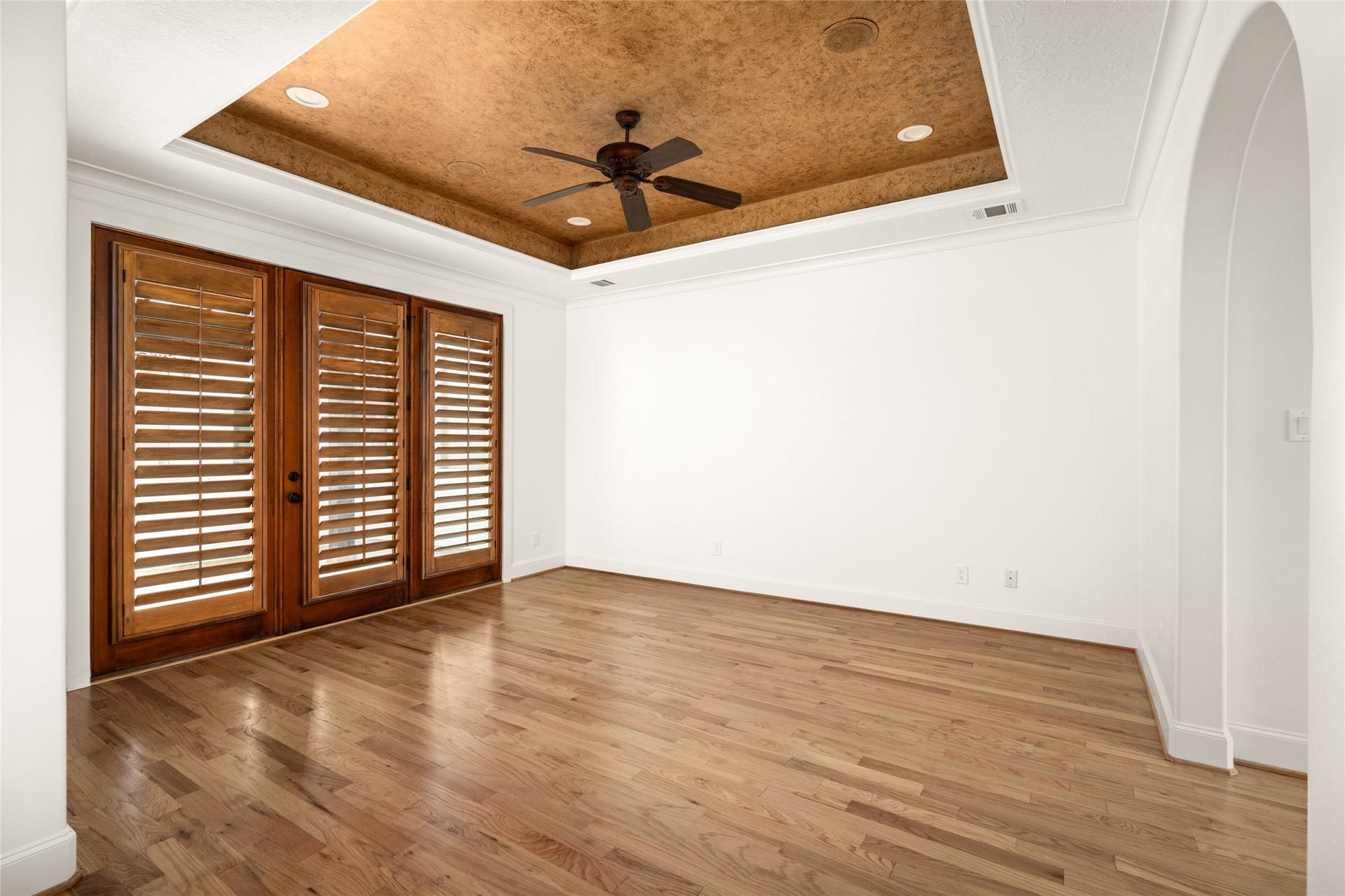 5218 Feagan Street, #D, Houston, TX 77007 Third floor - Spacious primary suite featuring hardwood flooring, plantation shutters, and a distinctive tray ceiling with a ceiling fan.