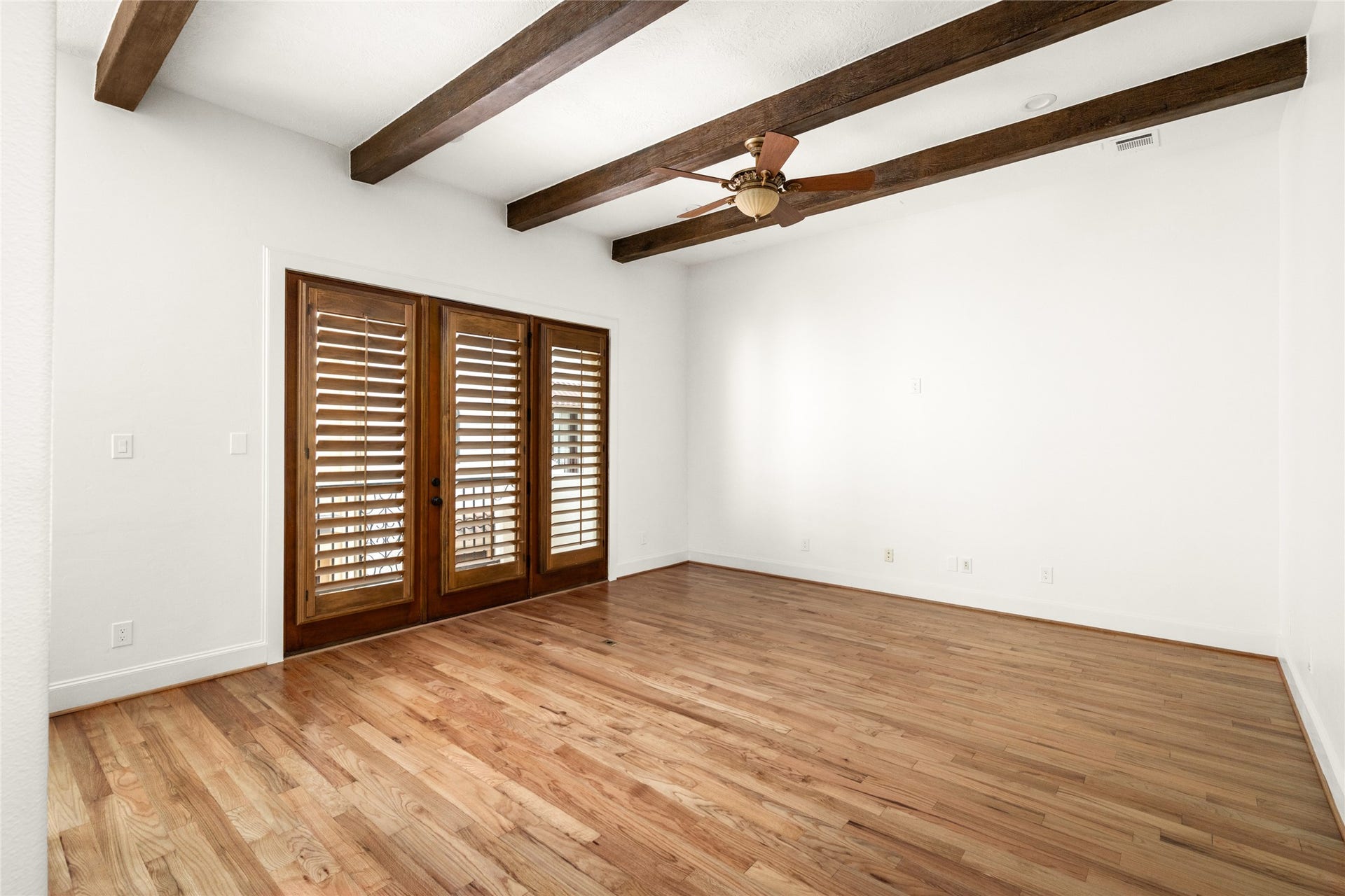 5218 Feagan Street, #D, Houston, TX 77007 Spacious second-floor living room featuring refinished oak hardwood floors, exposed wood ceiling beams, a ceiling fan, and French doors with plantation shutters.
