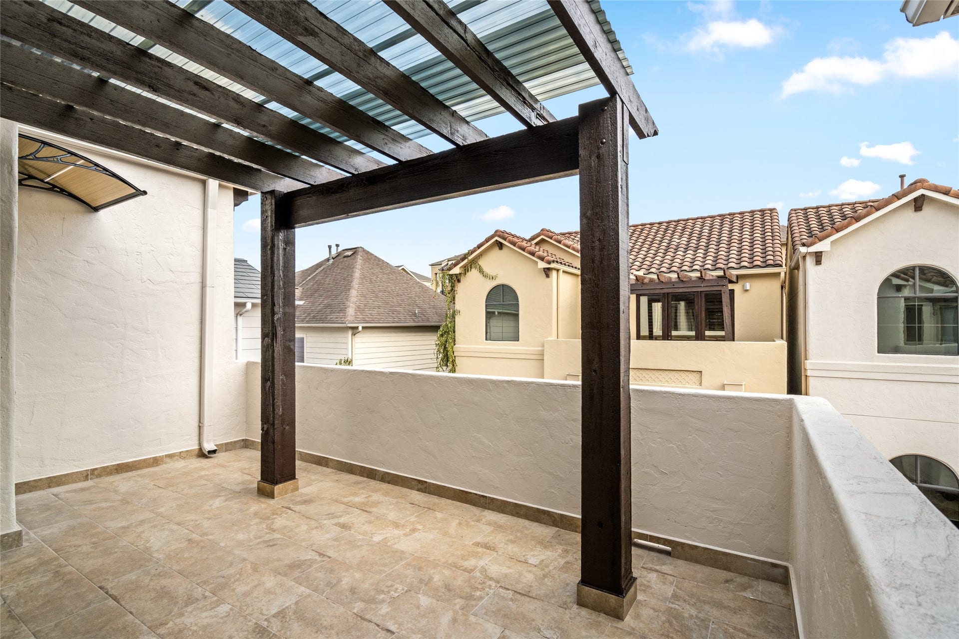 5218 Feagan Street, #D, Houston, TX 77007 Enjoy outdoor relaxation on the private covered balcony, featuring warm tile flooring, rustic wood pergola beams, and neighborhood viewsan inviting space to unwind and enjoy the fresh air.