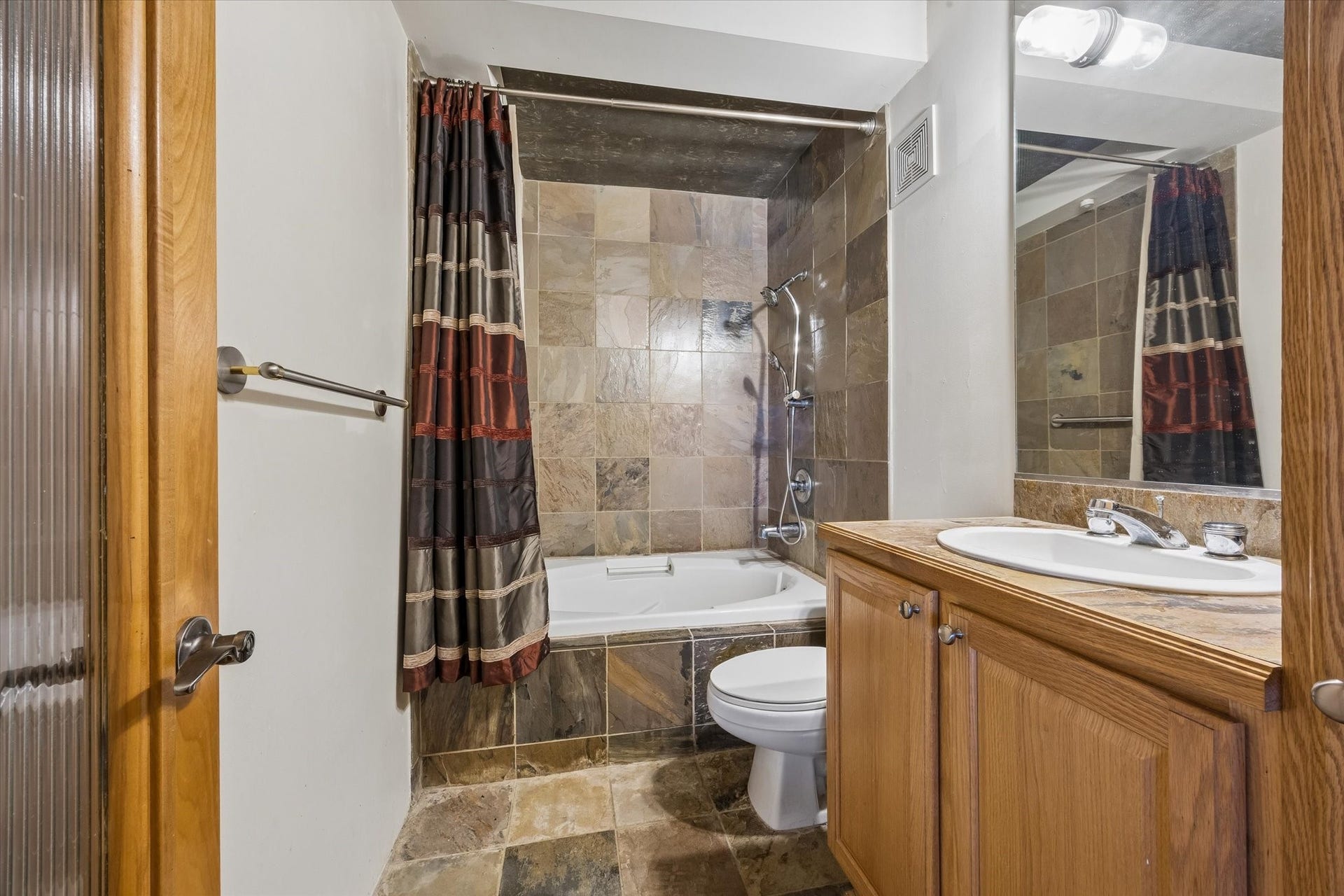 The bathroom features a spacious vanity with wood cabinetry, a large mirror, and a tub and shower combination. Neutral finishes and practical storage create a comfortable space for everyday routines.