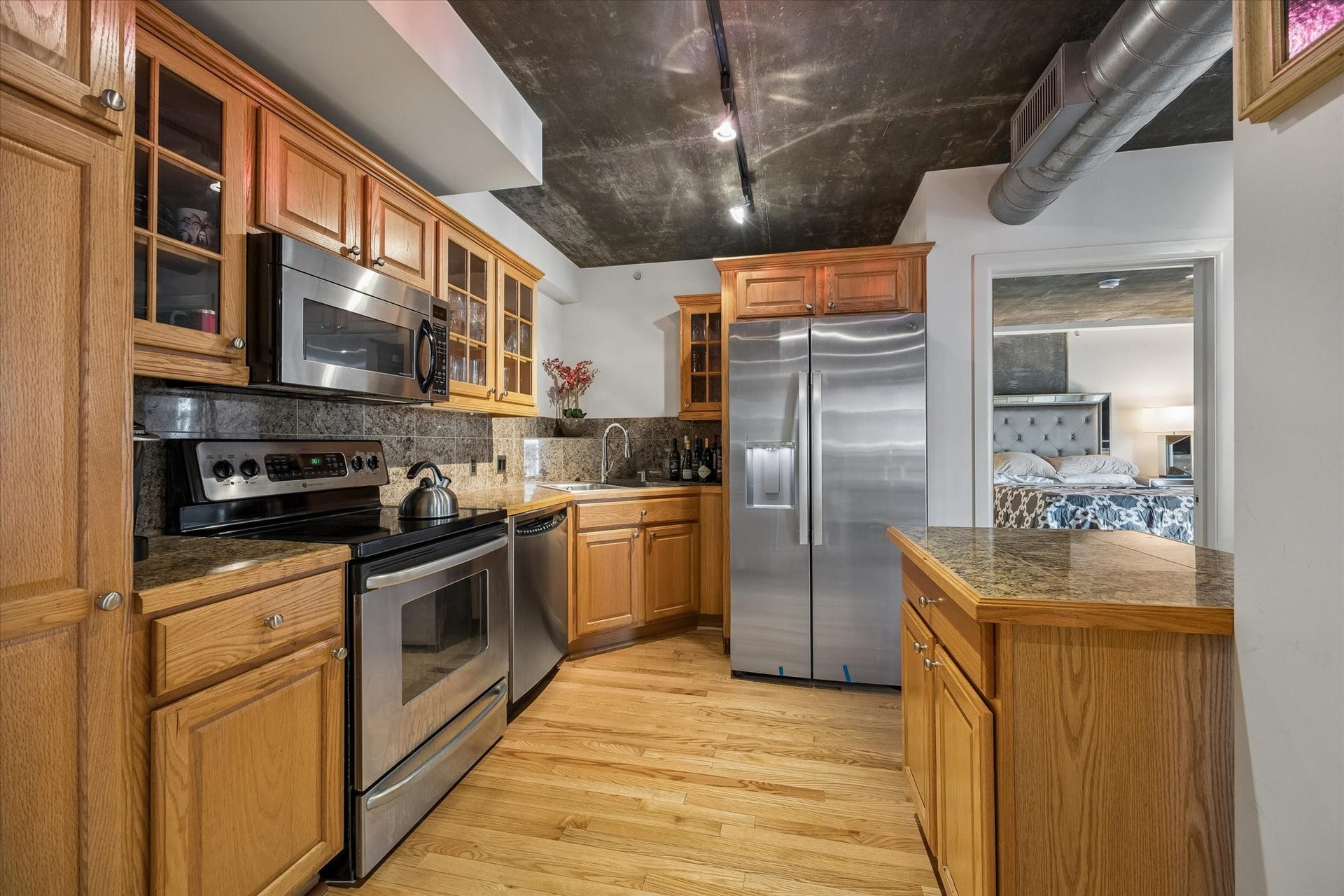 The kitchen features a center island, stainless steel appliances, and generous wood cabinetry for everyday functionality. Exposed concrete ceilings and industrial-inspired details give the space its distinctive loft aesthetic.