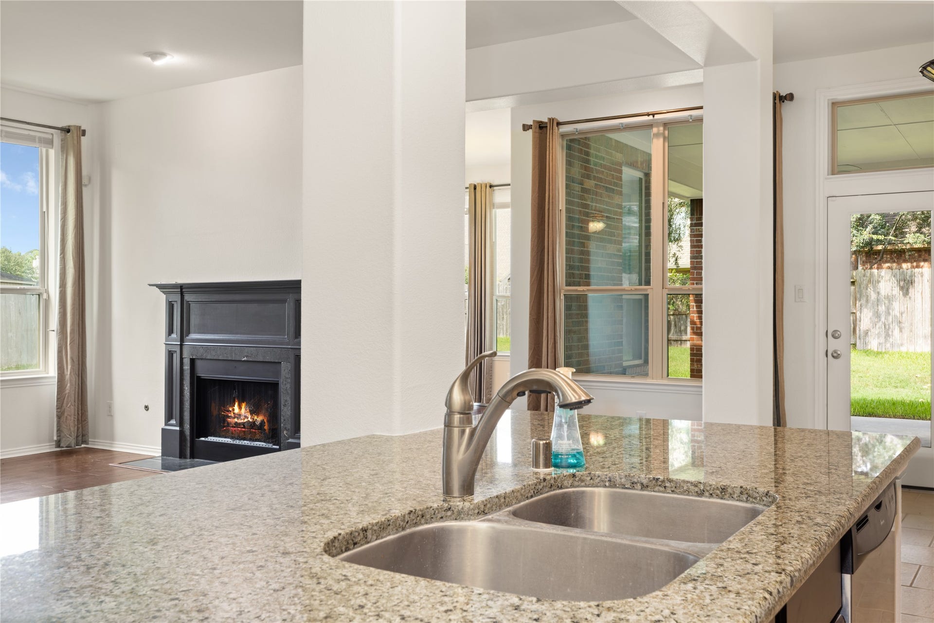 Elegant kitchen with granite countertops overlooks a cozy living area featuring a fireplace, and offers views of the lush backyard through large windows.