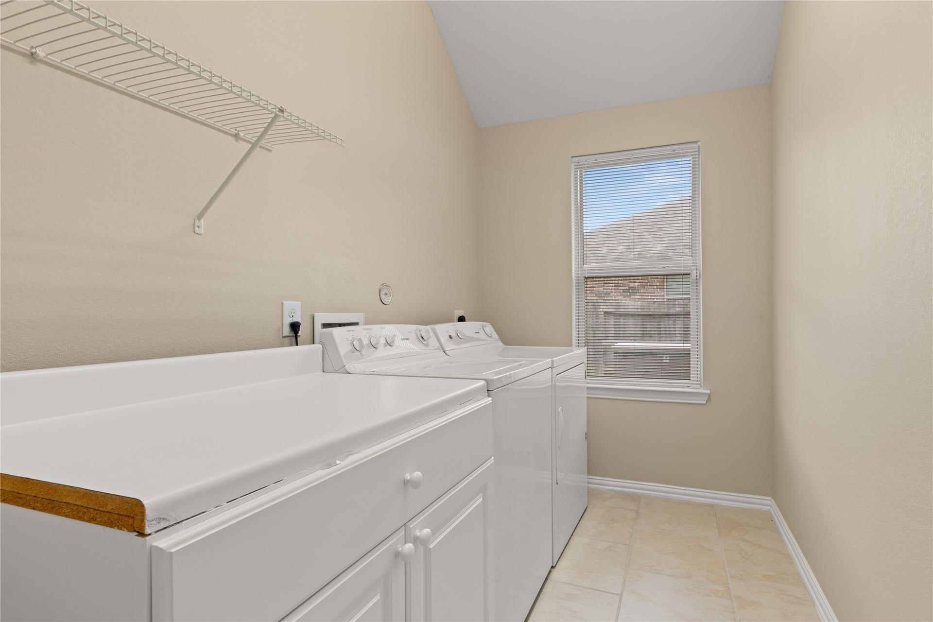 Bright laundry room featuring a washer and dryer set, ample counter space, and a window for natural light.