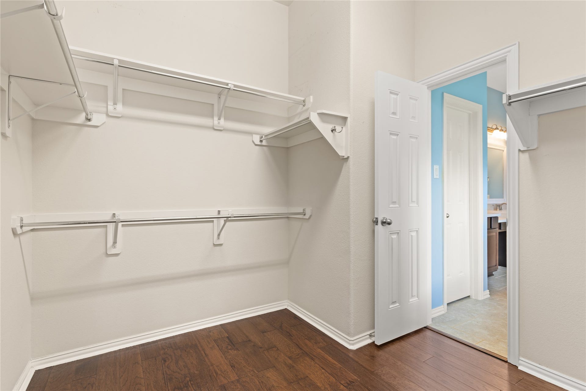 Spacious walk-in closet with ample shelving and hanging space, featuring hardwood floors and convenient access to an adjoining bathroom.