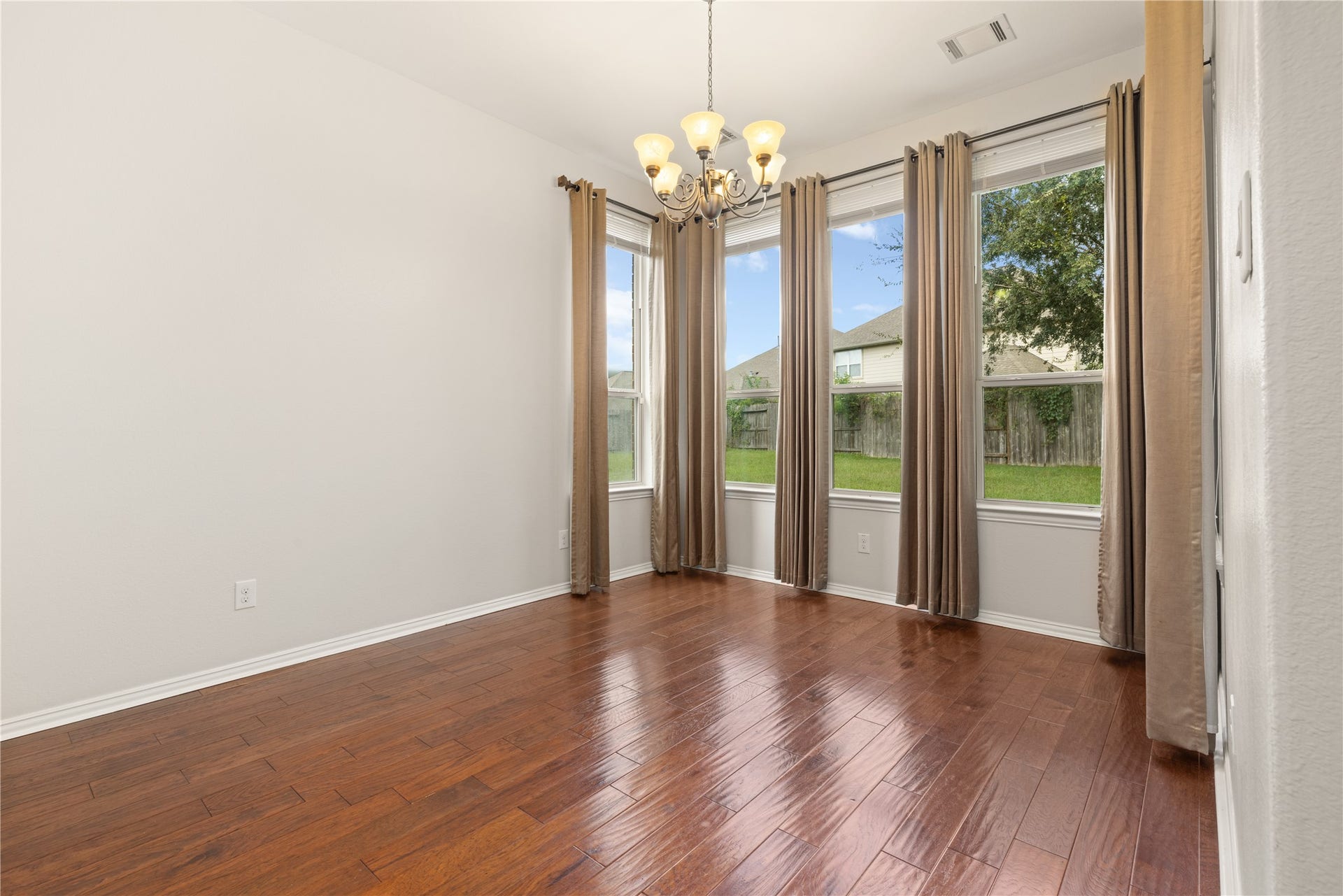 Bright dining area with rich wood flooring, large windows offering abundant natural light, and a classic chandelier.