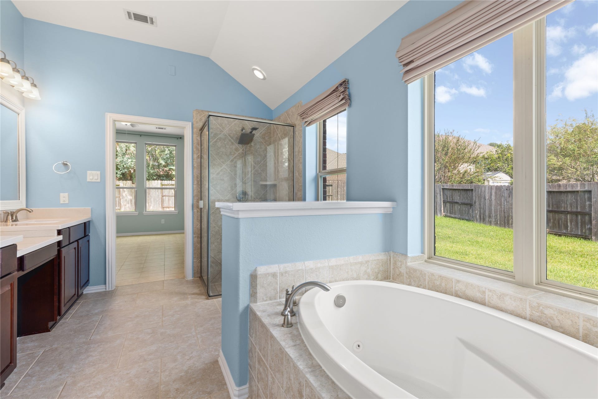 Bright and airy bathroom featuring a luxurious soaking tub with a view. Enjoy the spacious walk-in shower and dual vanities, all set against soothing blue walls.