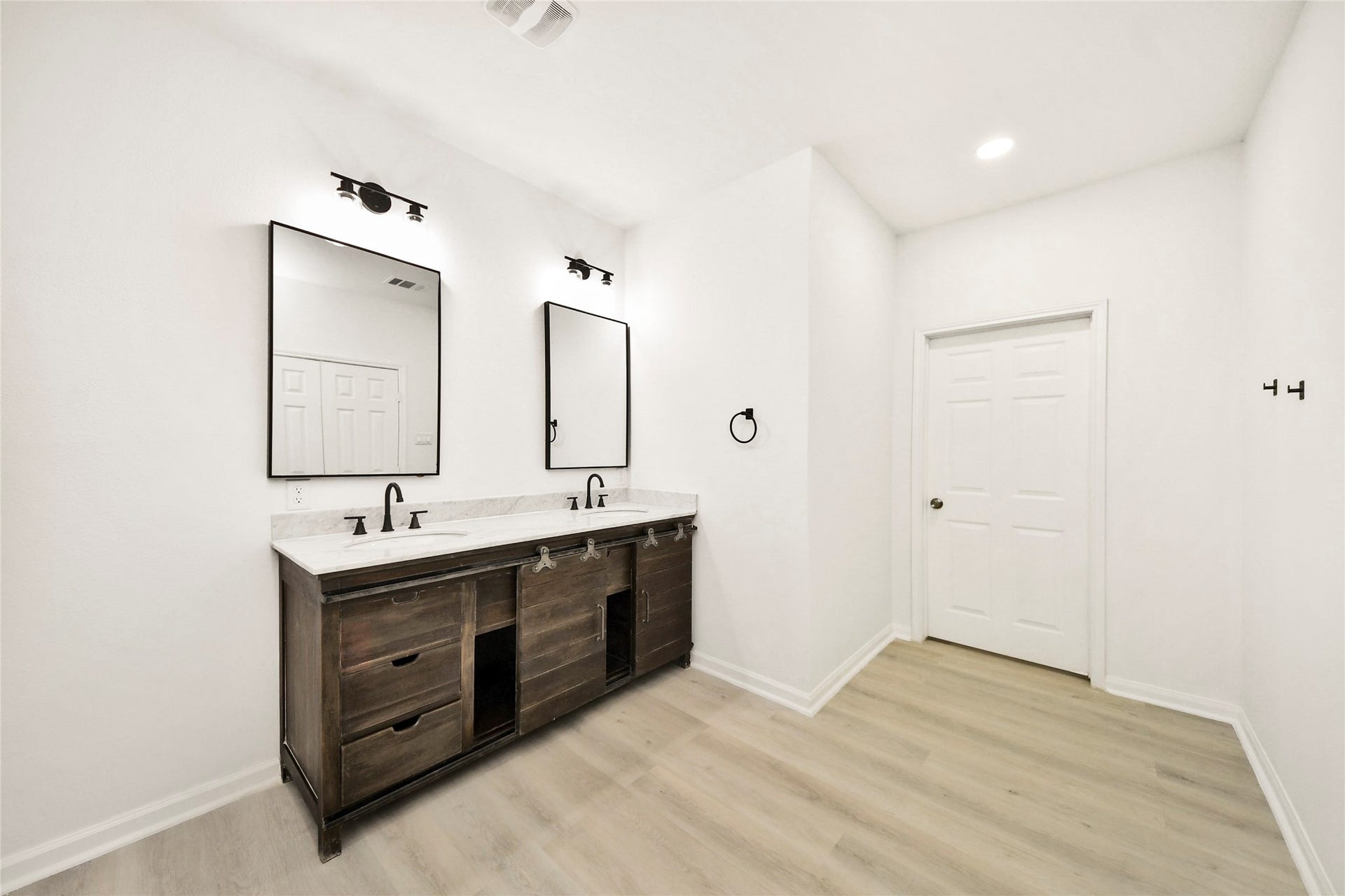 4615 Collingsworth Street, #AB, Houston, TX 77026 Spacious modern bathroom featuring a dual vanity with sleek black fixtures, elegant mirrors, and ample storage, complemented by light wood flooring and bright walls.