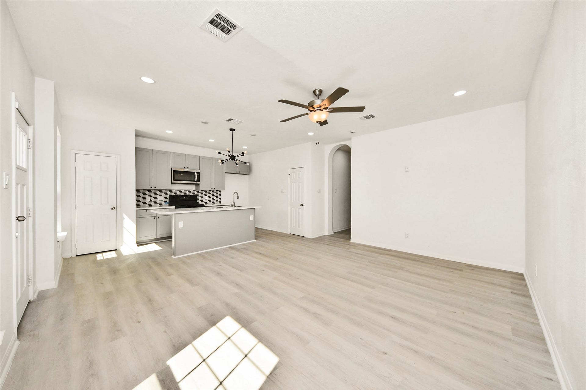 4615 Collingsworth Street, #AB, Houston, TX 77026 Spacious open-concept living area with sleek wood flooring, modern ceiling fan, and a stylish kitchen featuring a central island and contemporary backsplash.