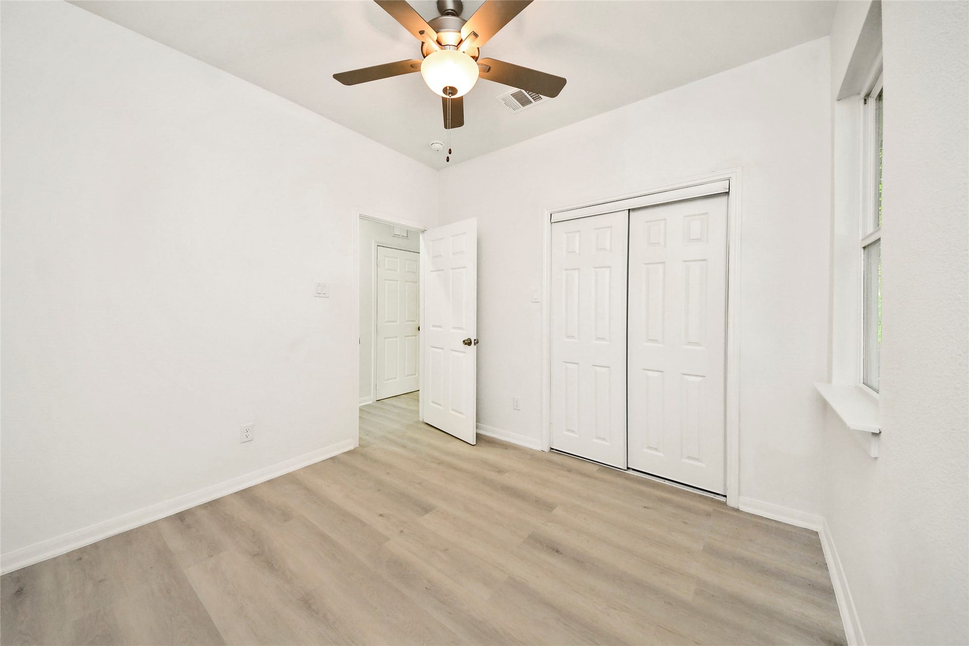 4615 Collingsworth Street, #AB, Houston, TX 77026 Bright and airy bedroom featuring fresh white walls, sleek laminate flooring, a modern ceiling fan, and ample closet space with double doors.