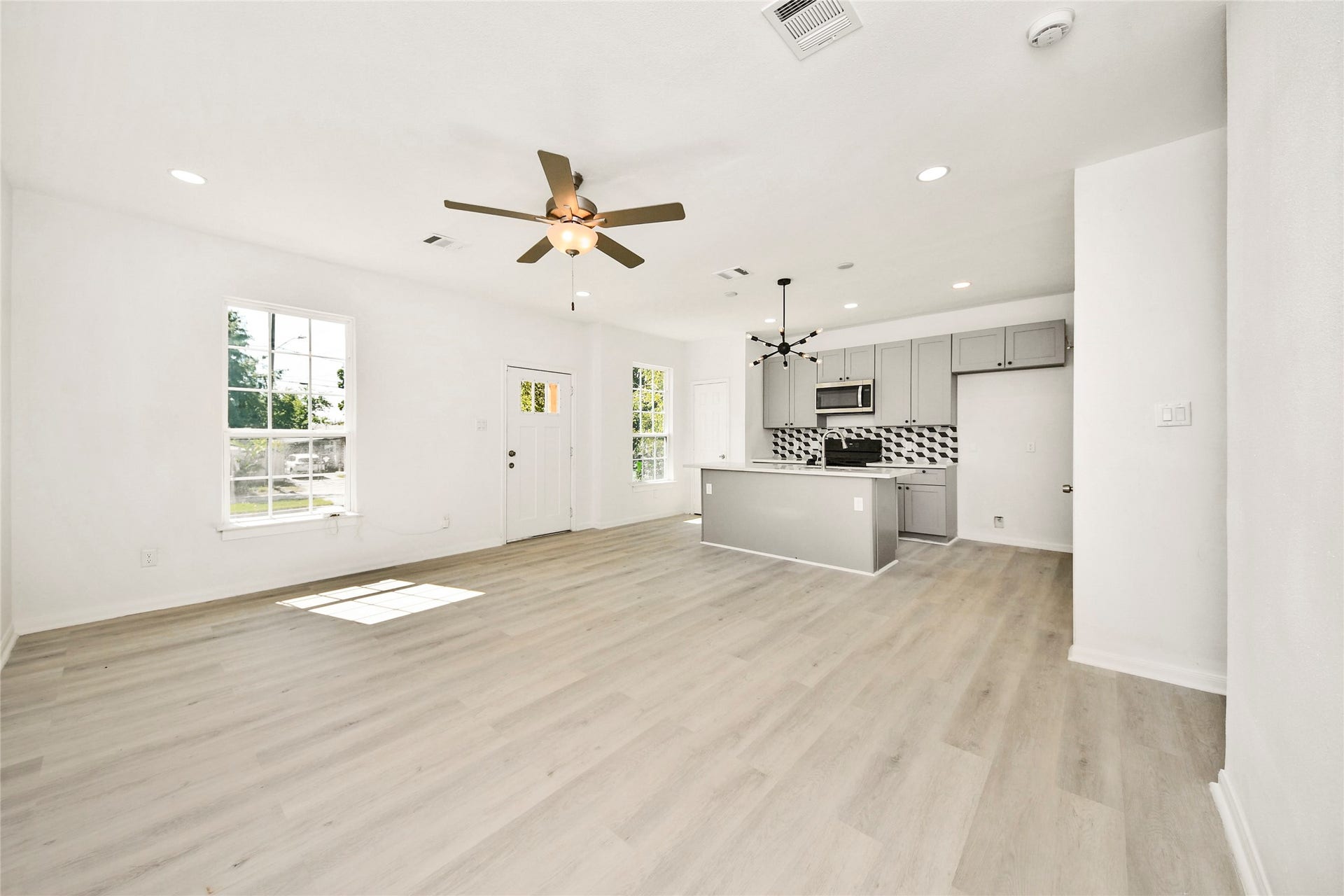 4615 Collingsworth Street, #AB, Houston, TX 77026 Bright and spacious open-concept living area featuring light wood flooring, modern ceiling fan, and a sleek kitchen with gray cabinetry and a stylish geometric backsplash.