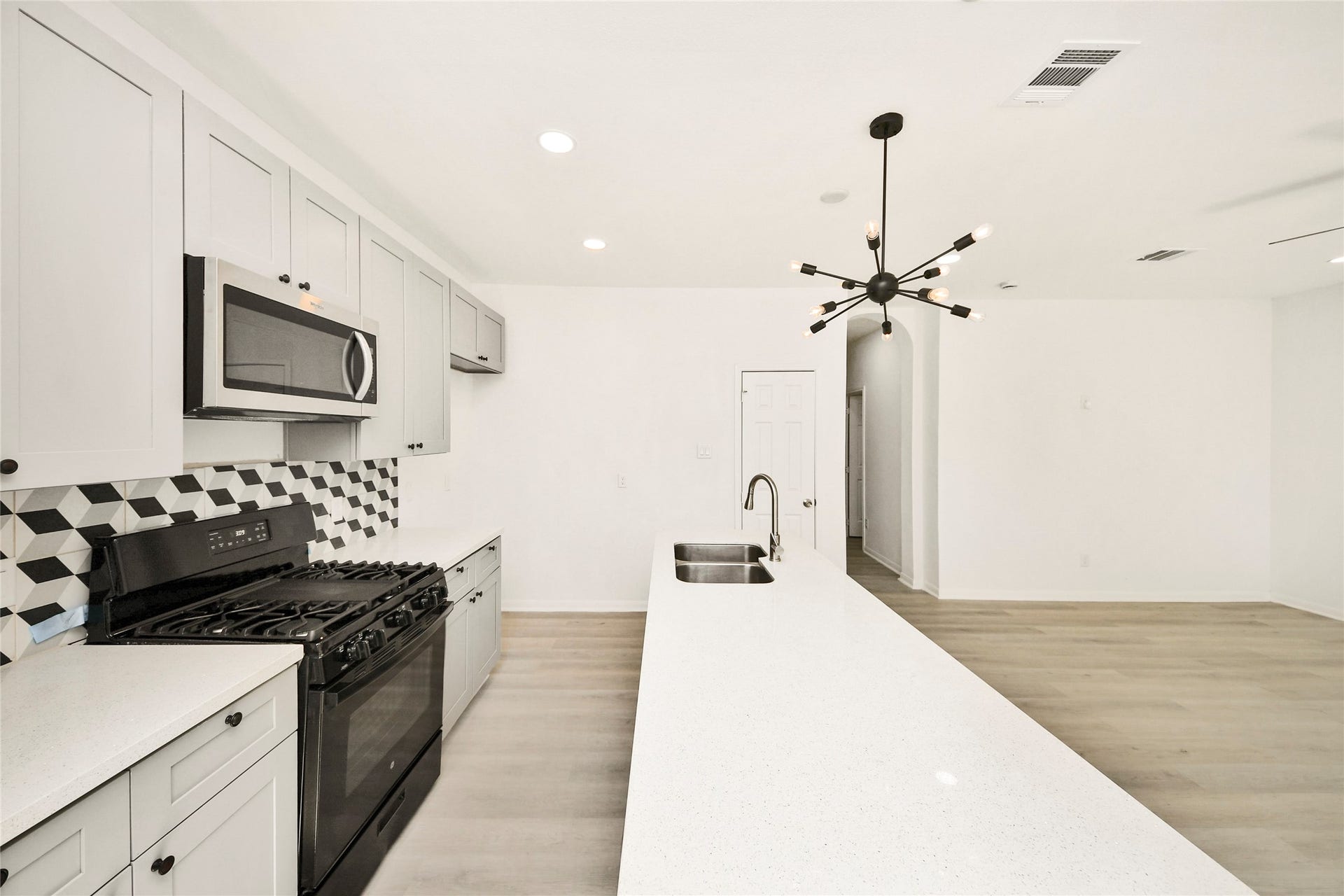 4615 Collingsworth Street, #AB, Houston, TX 77026 Sleek modern kitchen featuring a spacious island with a double sink, stylish geometric backsplash, and stainless steel appliances, all under a striking contemporary light fixture.